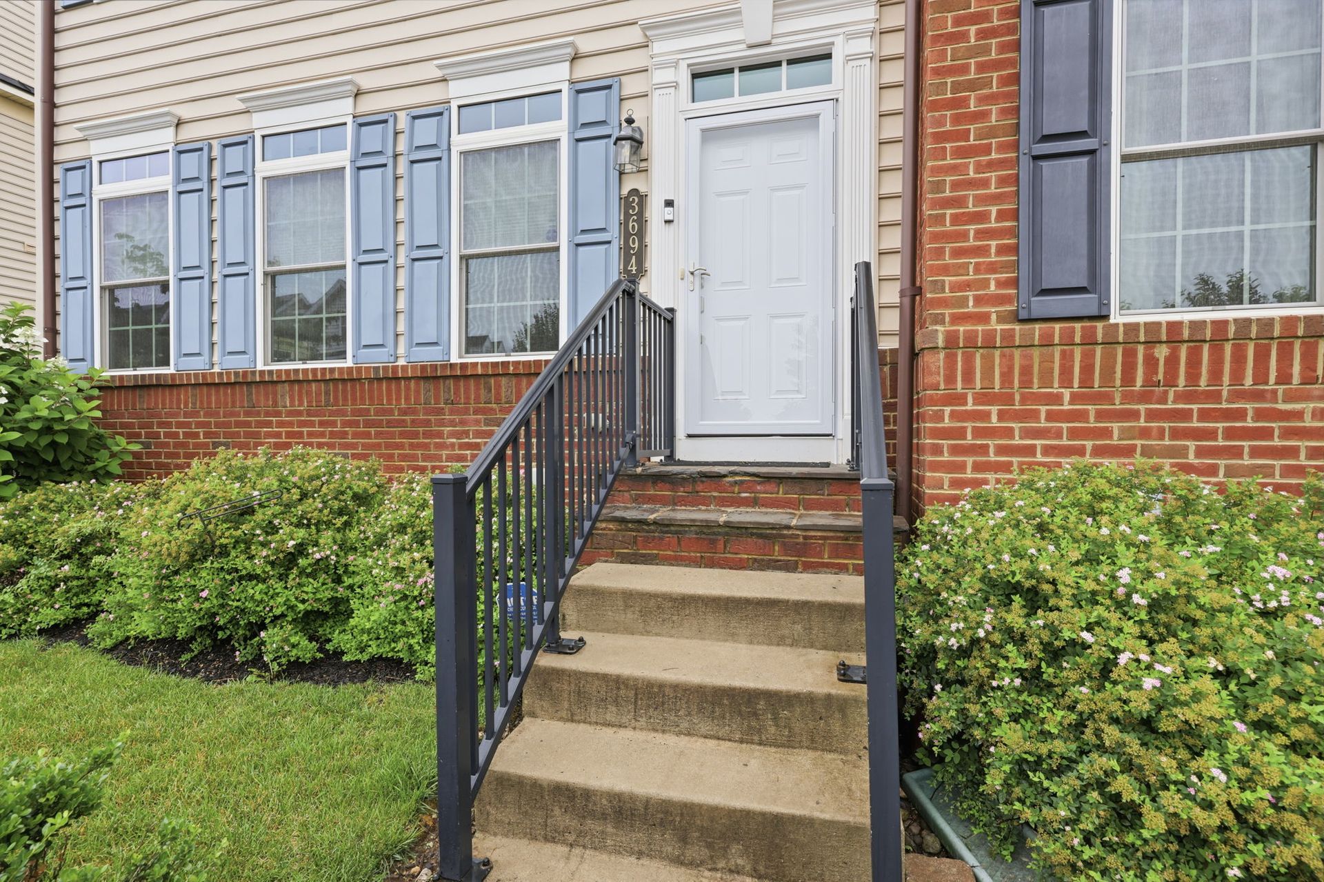 Front steps with black railings leading to a white townhouse door beside brick and siding walls.