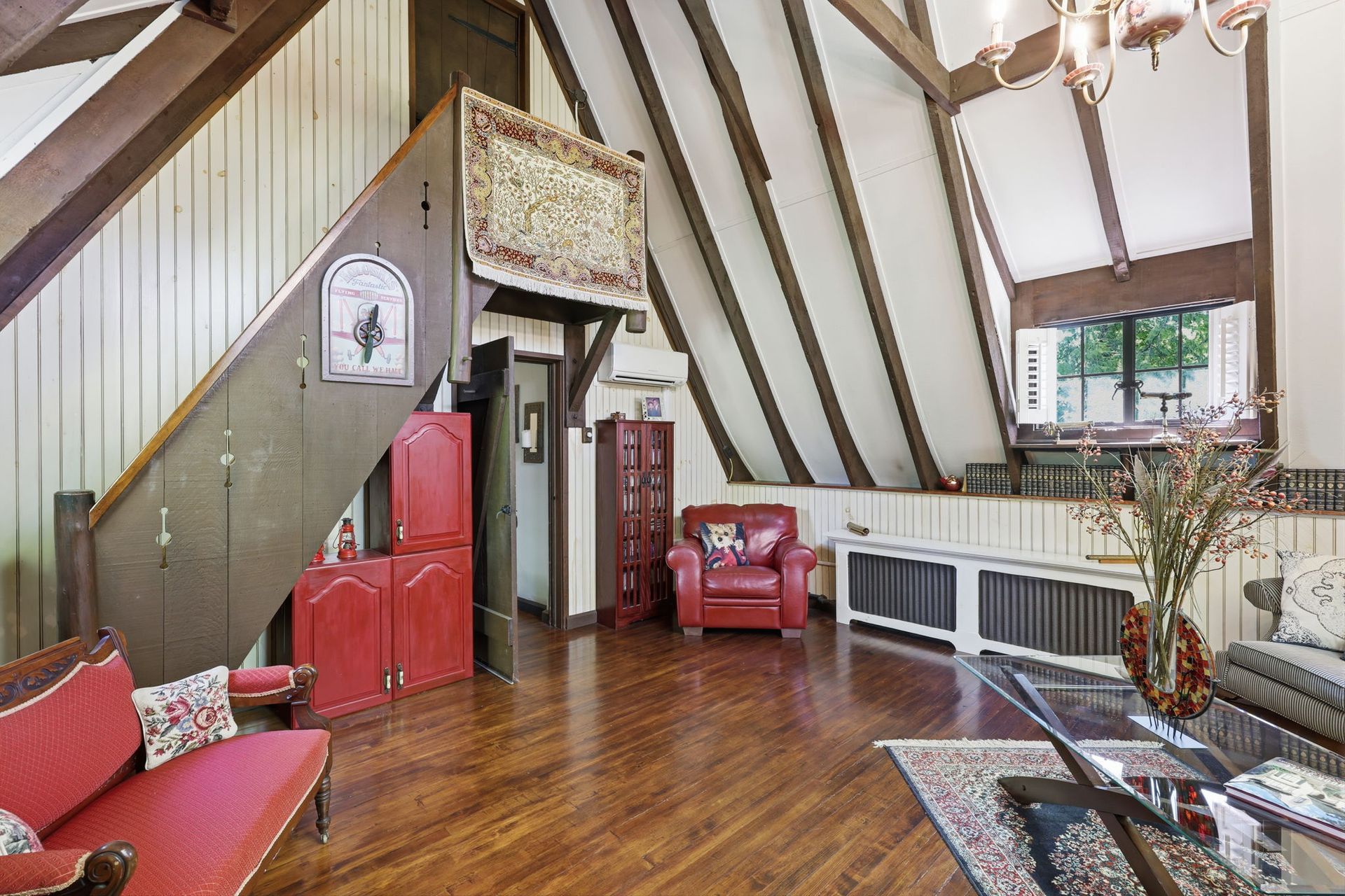 Cozy attic living room with wood floors, red chairs, skylight windows, and slanted beams