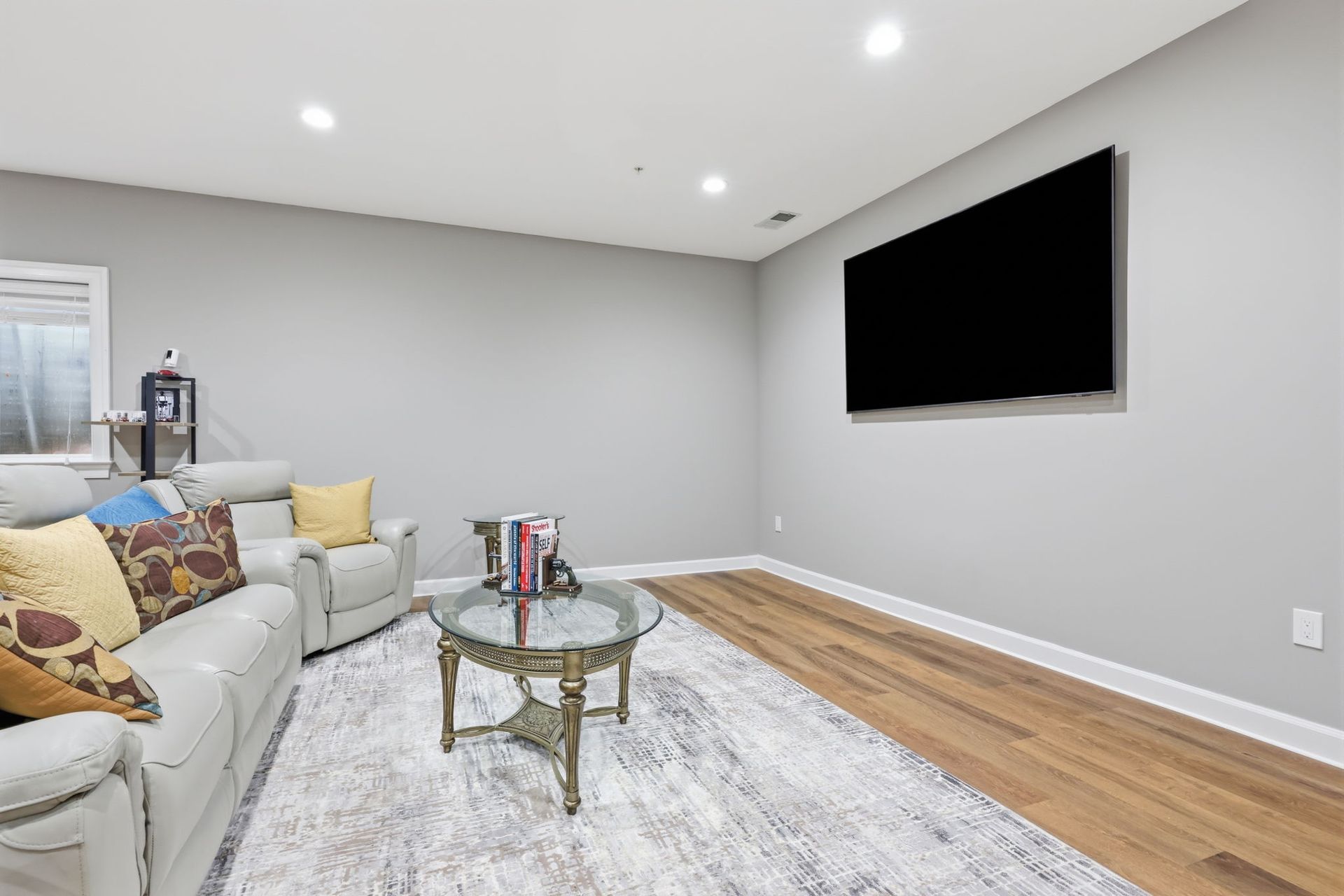 Modern living room with beige sectional, glass coffee table, wall-mounted TV, and wood flooring