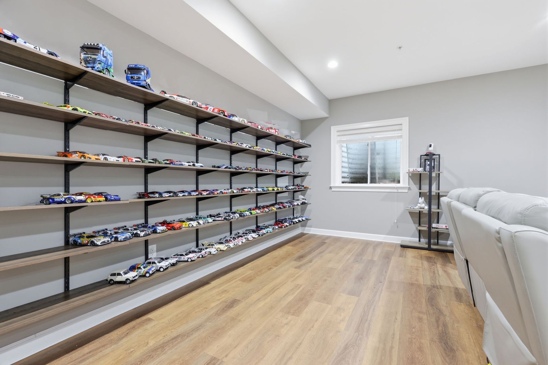 Modern room with wall-mounted shelves full of toys, wood floors, a window, and a white sofa