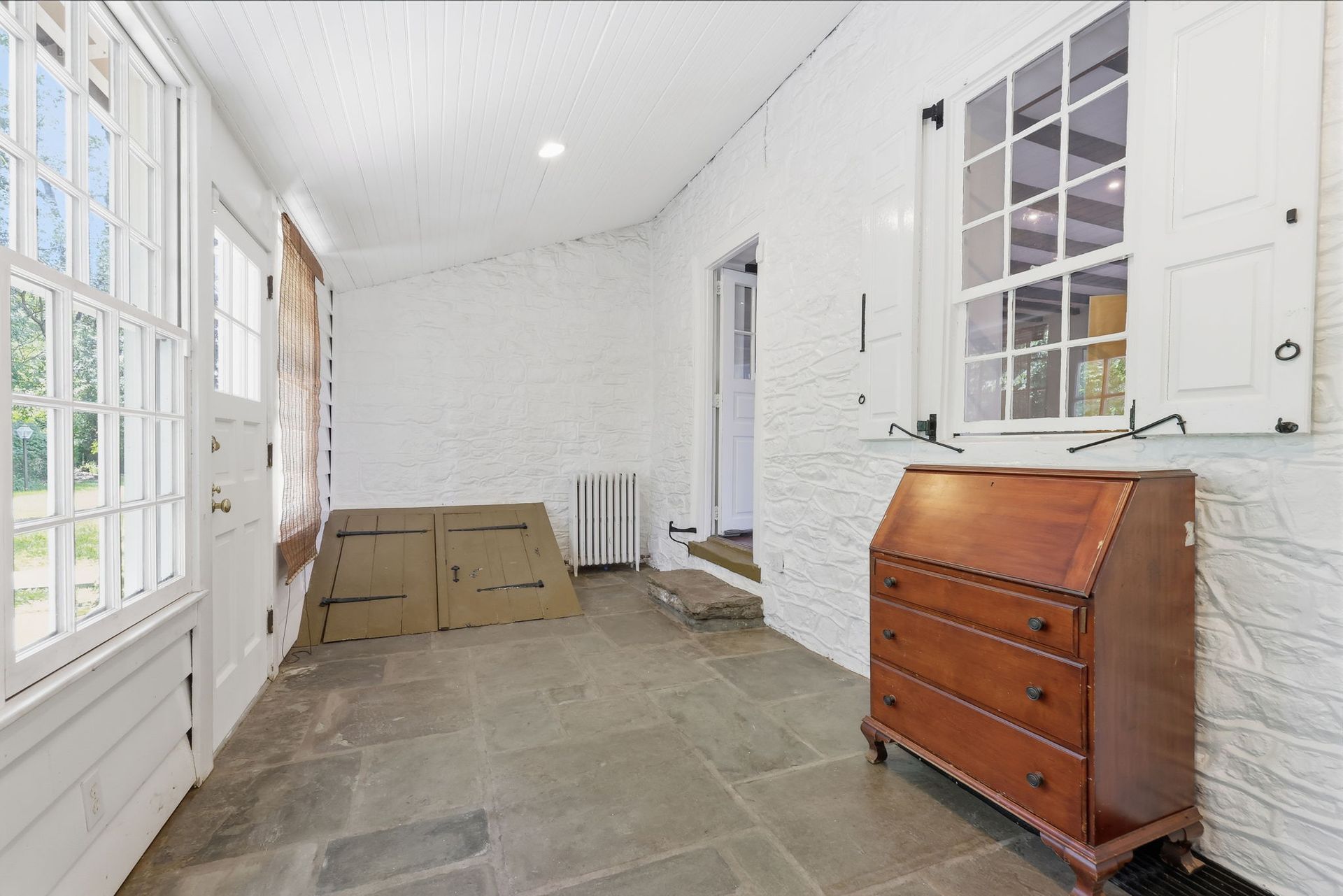 White hall with stone floor, windows, a wooden dresser, and stacked cardboard boxes near the back.