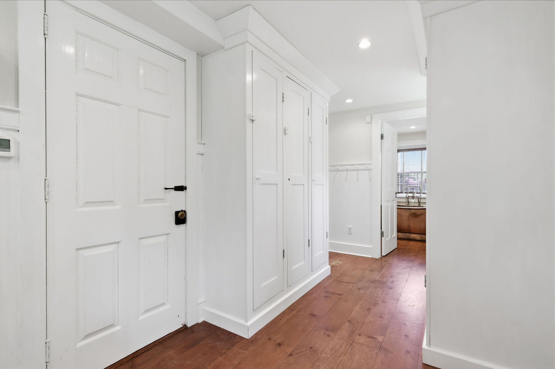 Bright white hallway with paneled doors and wood floor leading to a sunlit room.