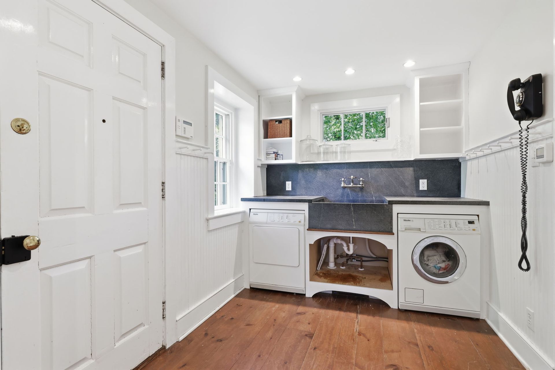 Small laundry room with white cabinets, blue tile backsplash, sink, and a front-loading washer.