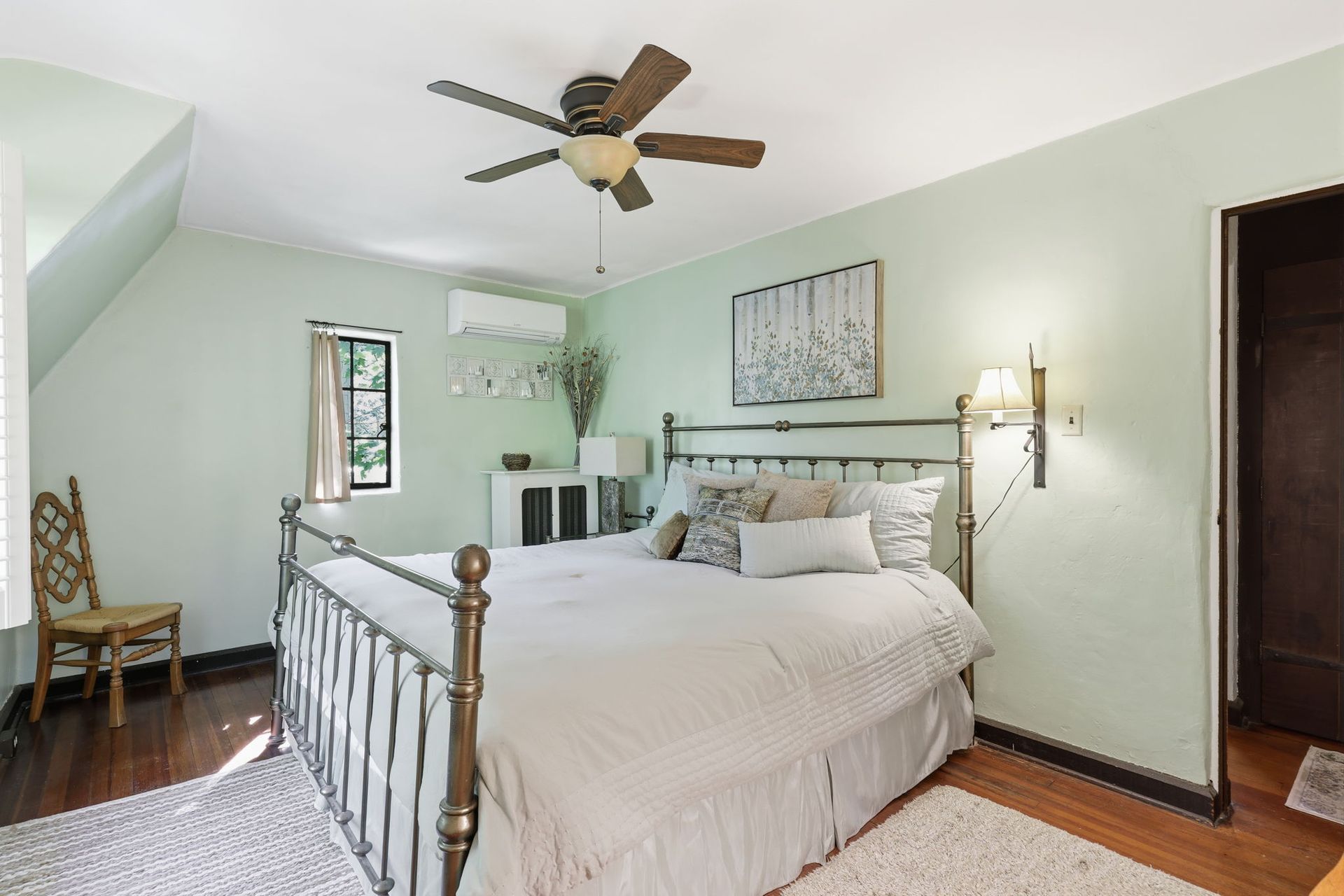 Bright bedroom with a wrought-iron bed, ceiling fan, and light green walls