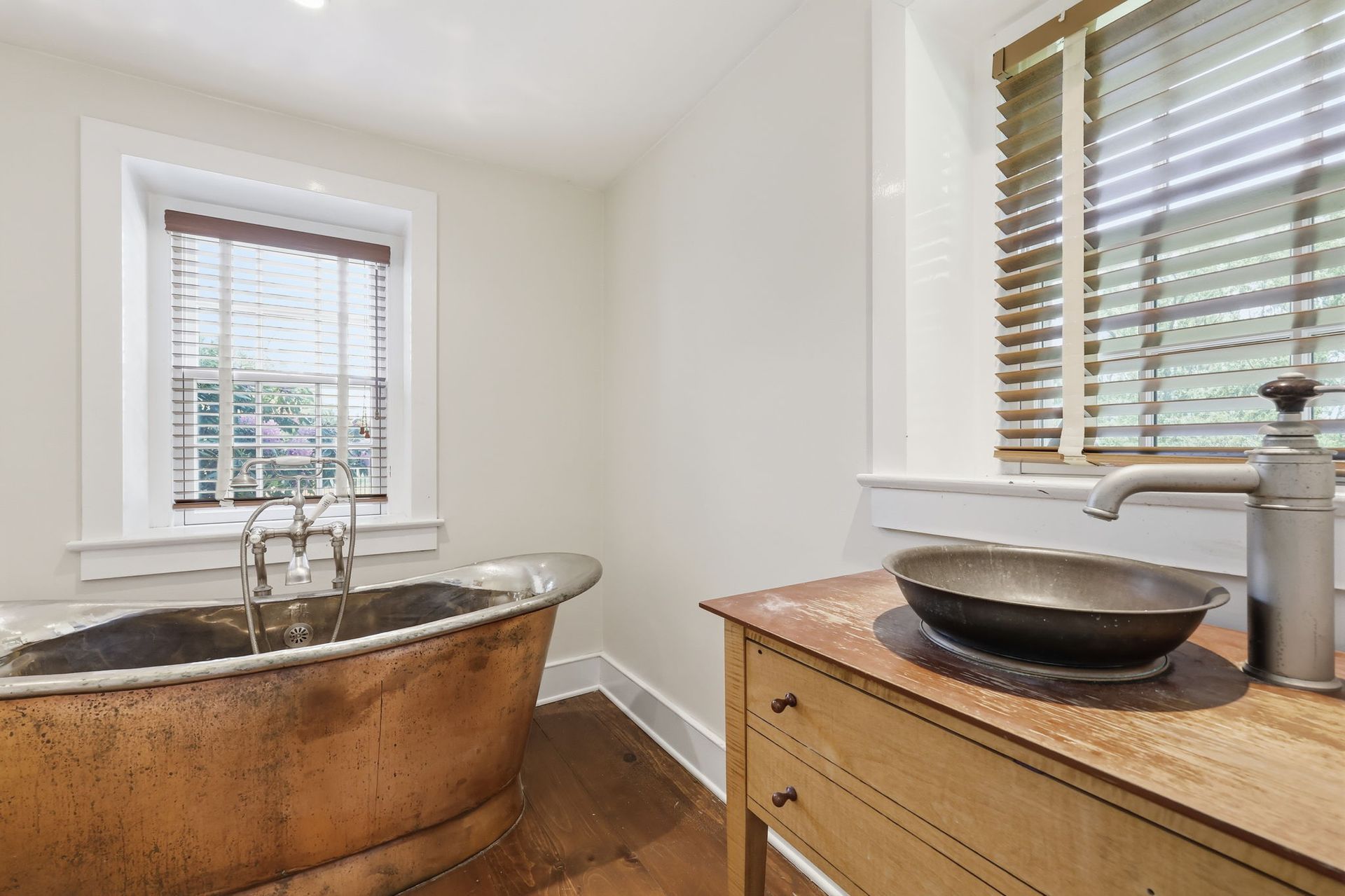 Bright bathroom with copper bathtub, window blinds, and wooden vanity with sink