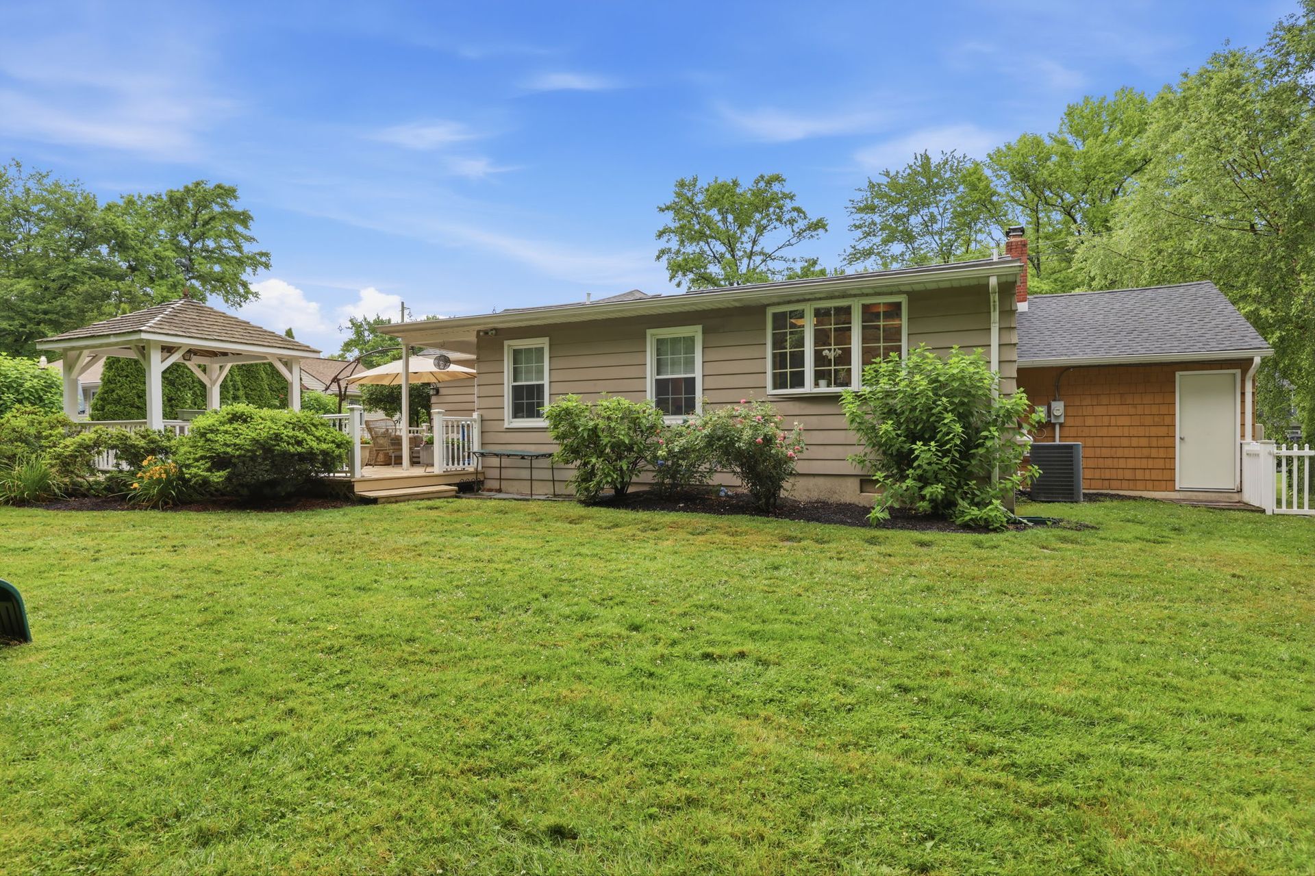Single-story tan house with a front porch, gazebo, and large green lawn under a blue sky