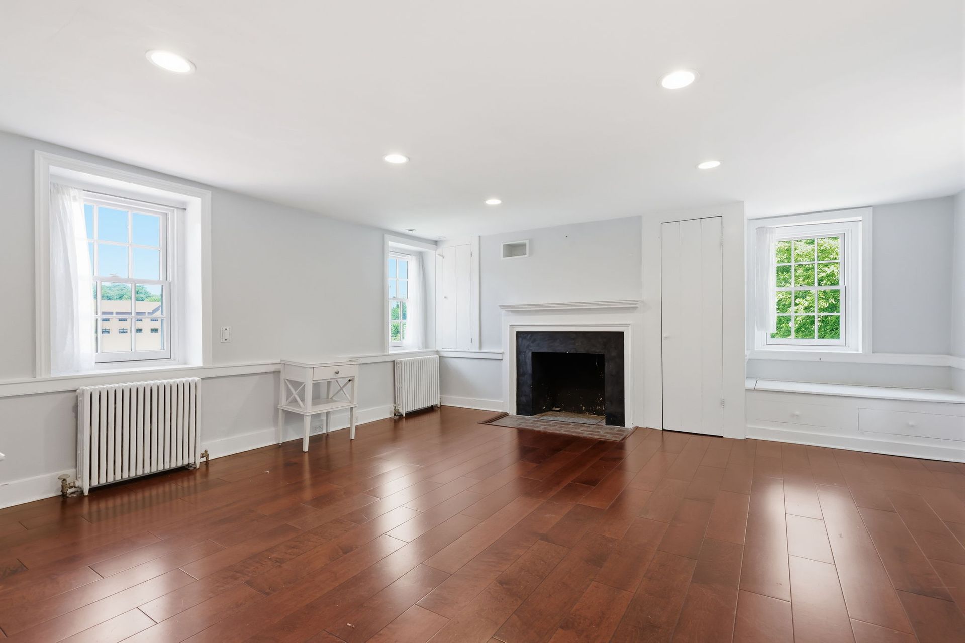 Bright empty living room with hardwood floors, white walls, fireplace, and windows letting in natural light