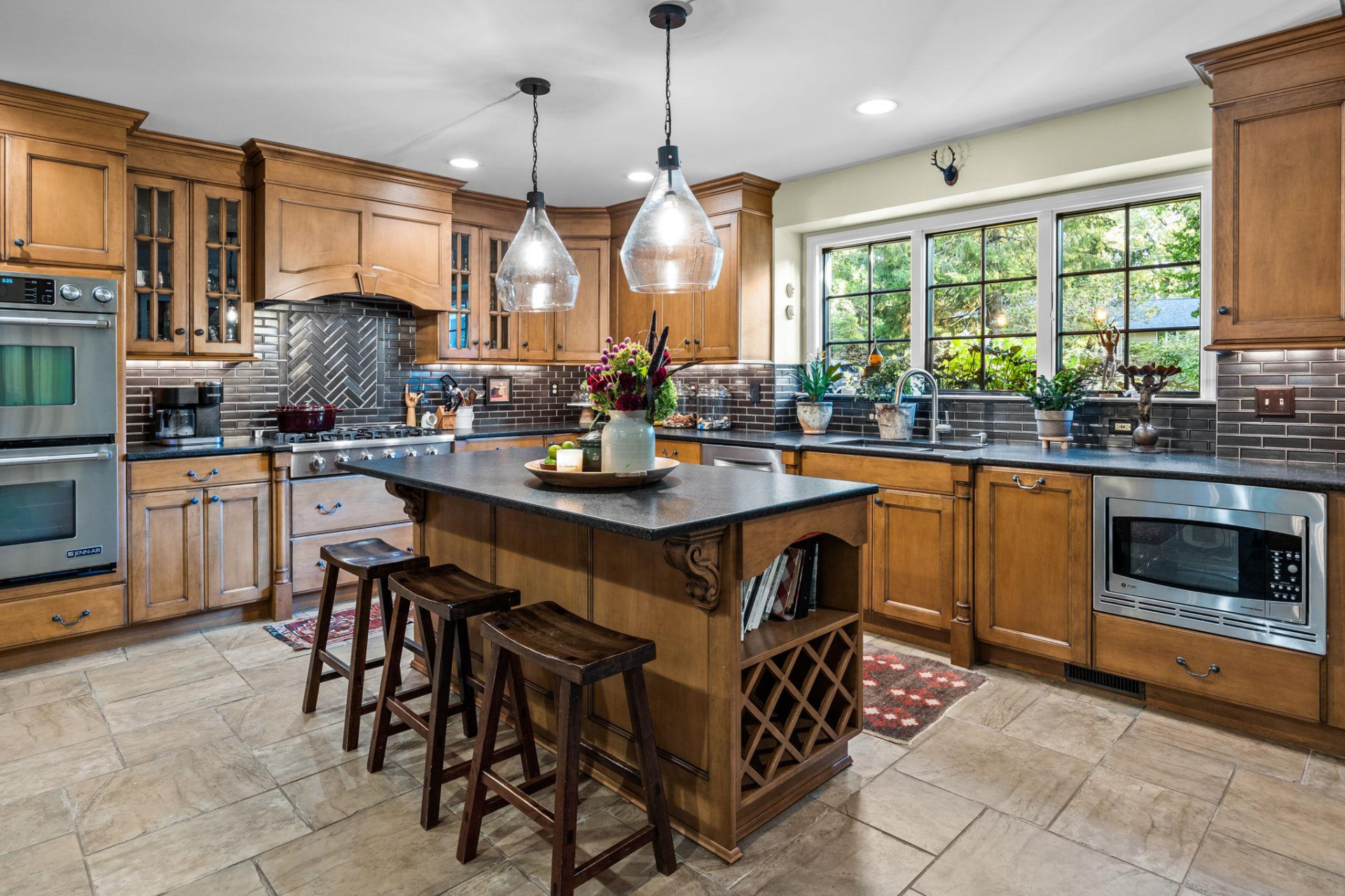 Kitchen with wooden cabinets, island with stools, and window overlooking trees.