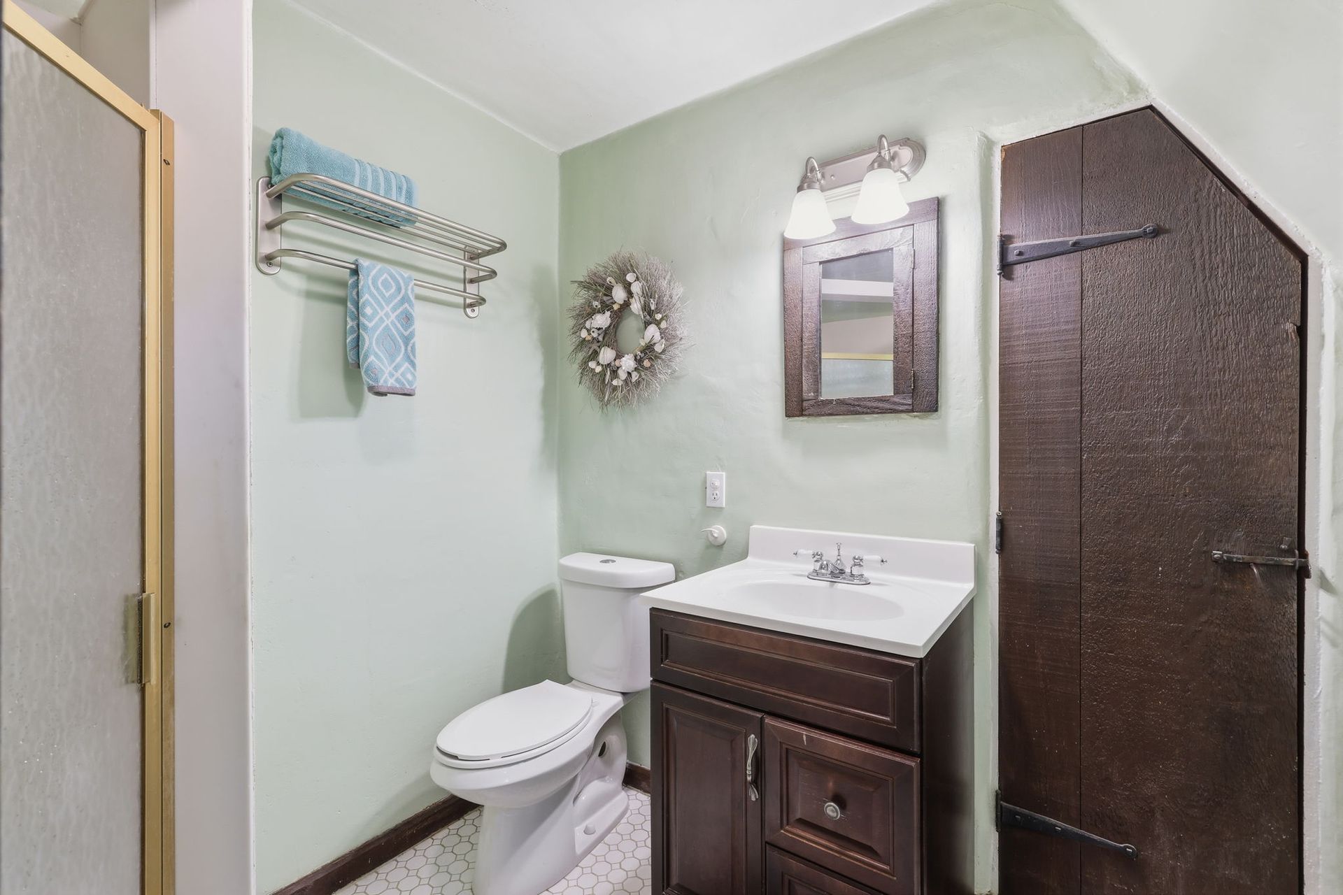 Small bathroom with toilet, vanity sink, towel rack, mirror, and brown door.