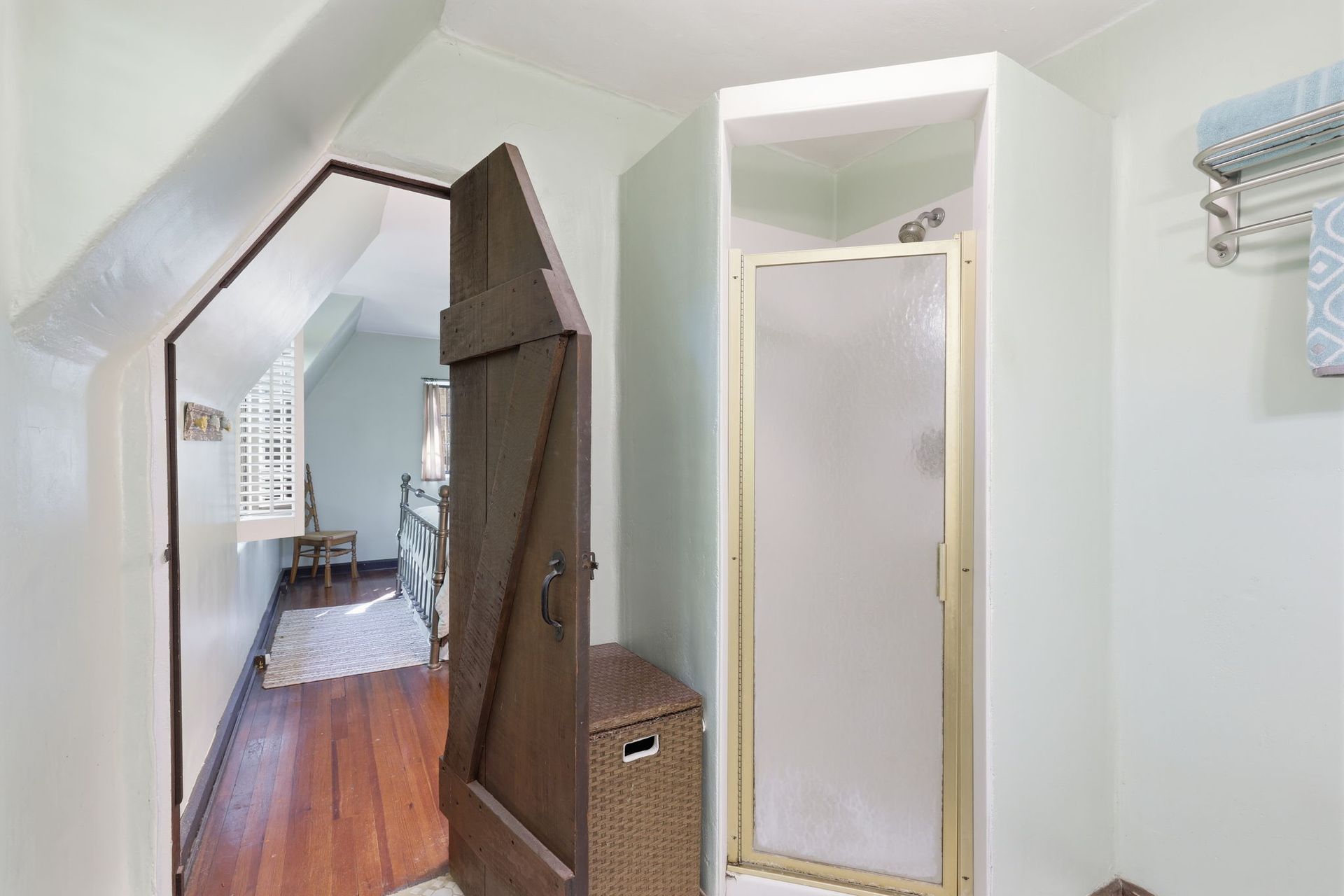 Bright hallway with a narrow glass shower door, wooden floor, and open door leading to a room.