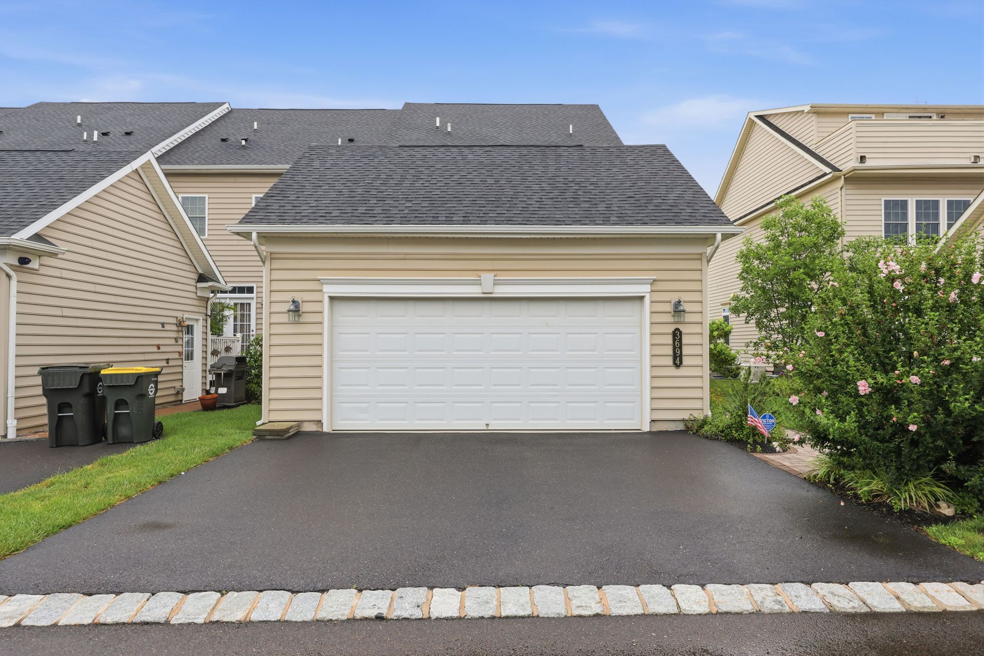 Single-story beige house with a two-car garage and dark driveway under a cloudy sky