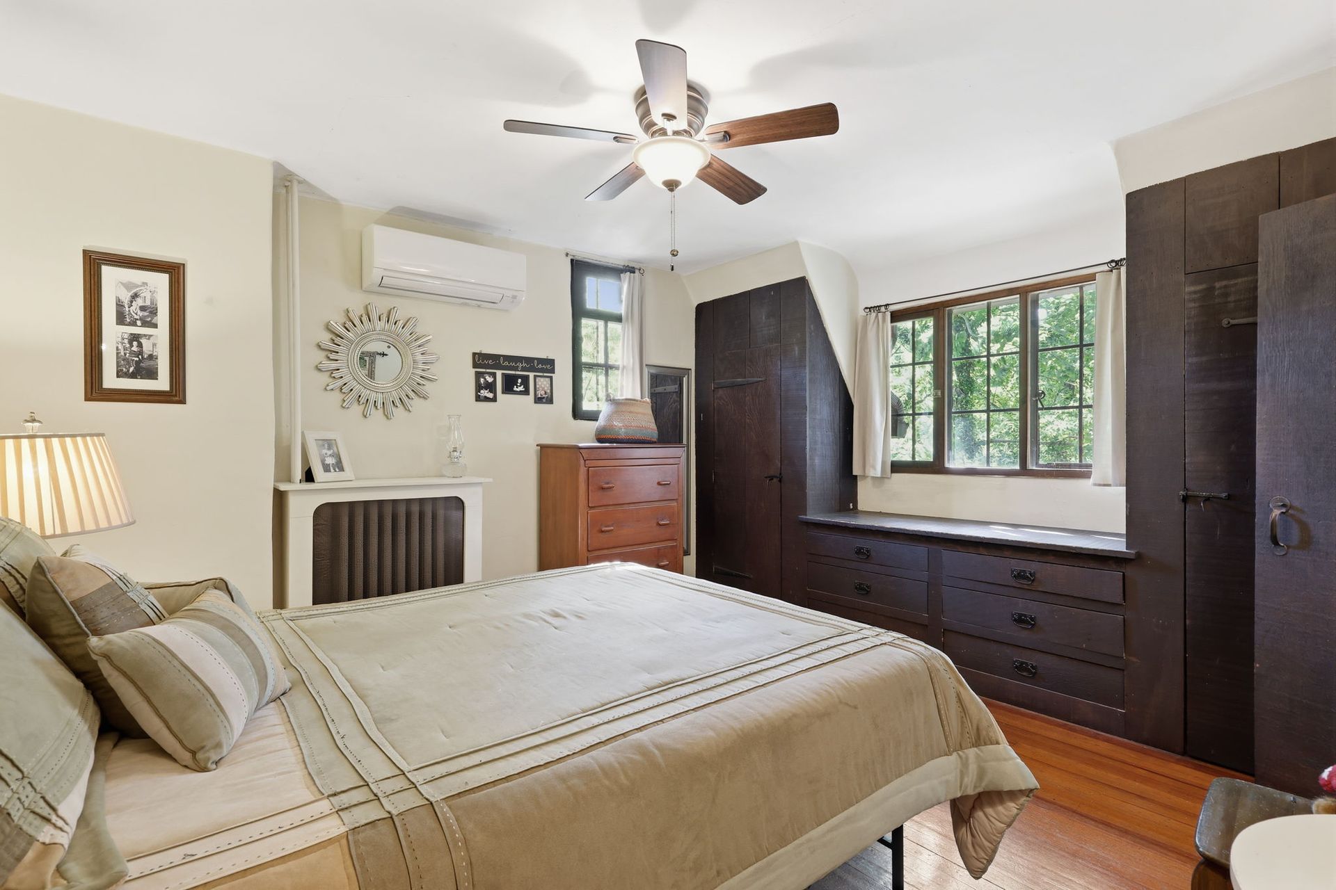 Cozy bedroom with beige bed, dark wood dresser, window, ceiling fan, and hardwood floor