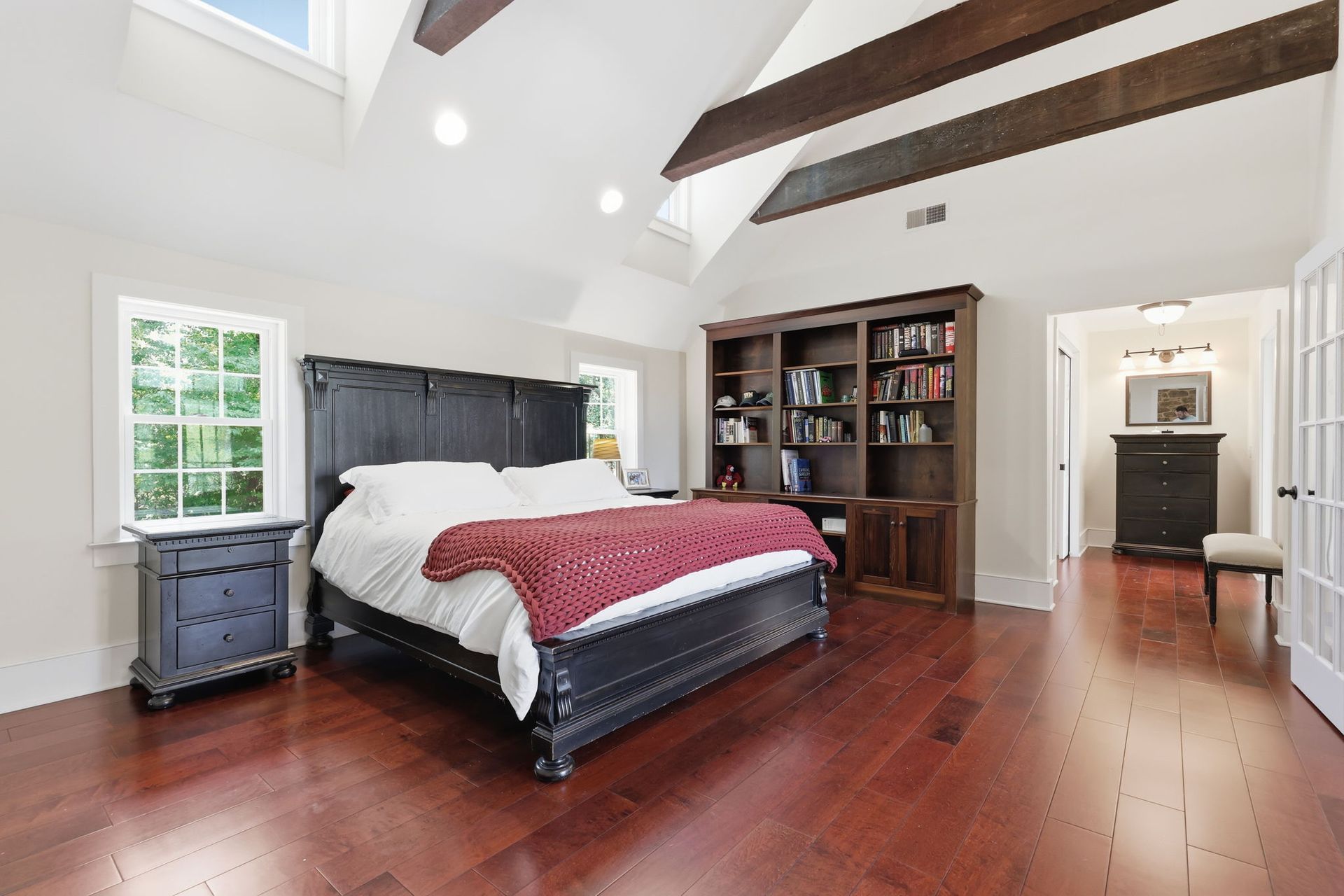 Bright bedroom with vaulted ceiling, dark wood floors, bed, dresser, bookshelf, and skylight lights
