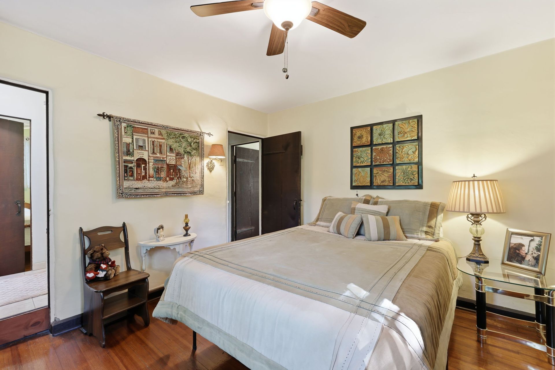 Cozy bedroom with a bed, wood floor, ceiling fan, lamps, and framed wall art