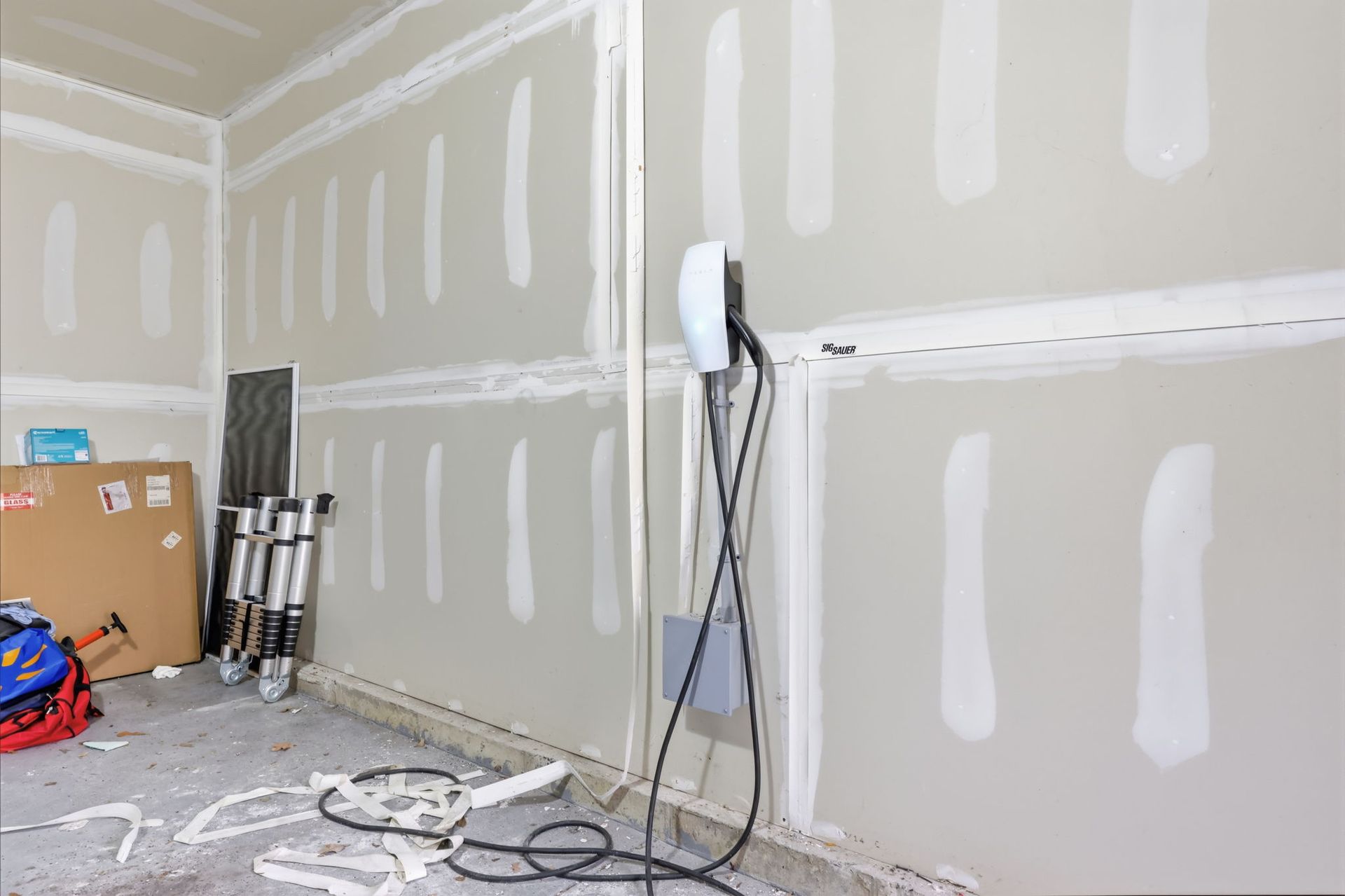 Unfinished drywall room with taped seams, a standing fan, cords, and construction supplies on the floor.