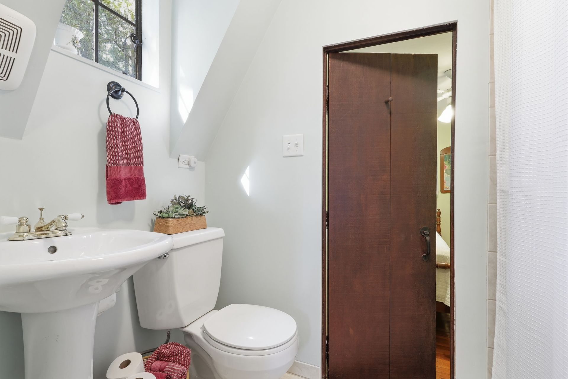 Small bathroom with white sink and toilet, red accents, and an open wooden door