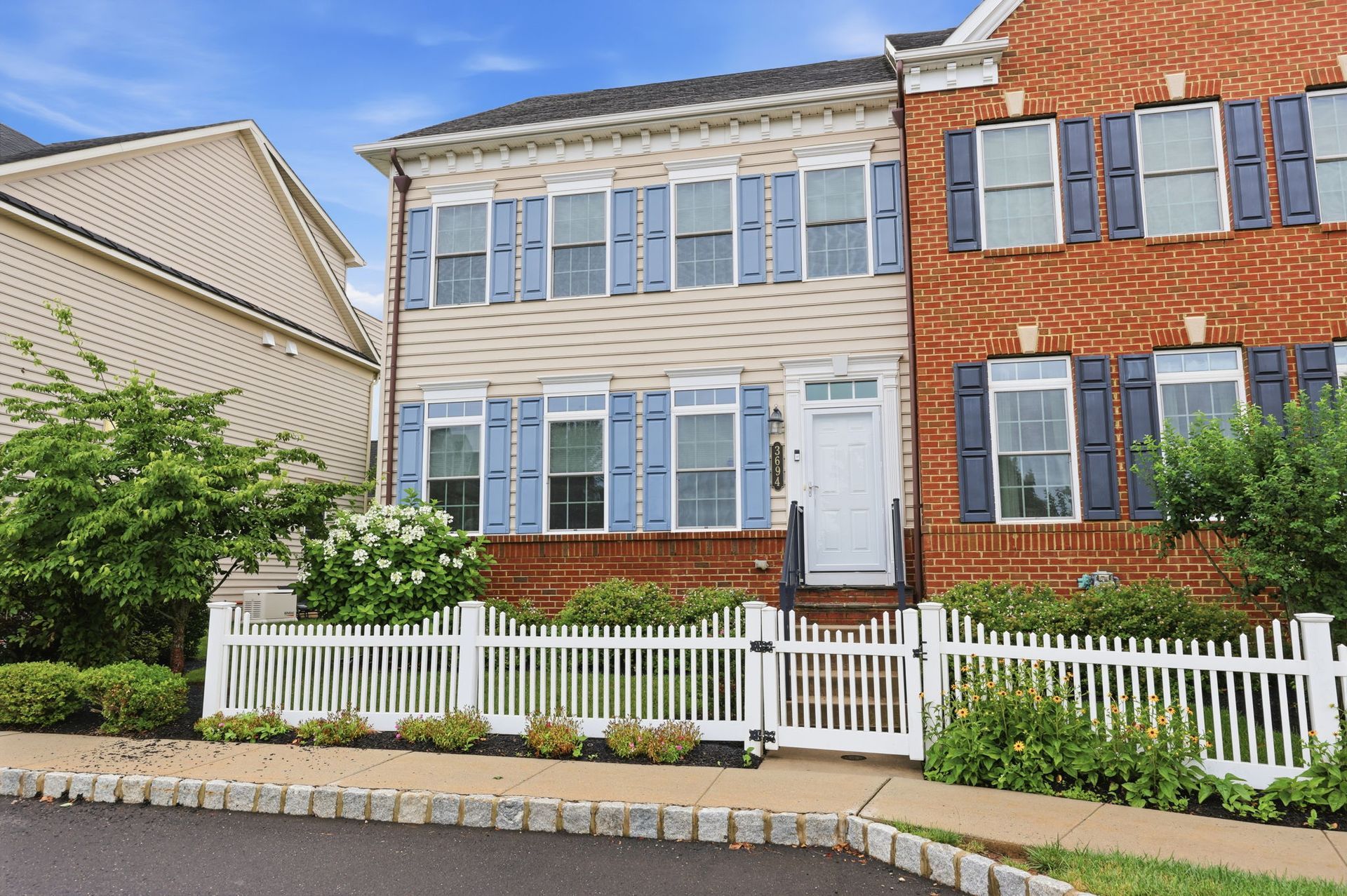Row of suburban houses with white picket fences, including a beige home and a red brick home on a sunny day