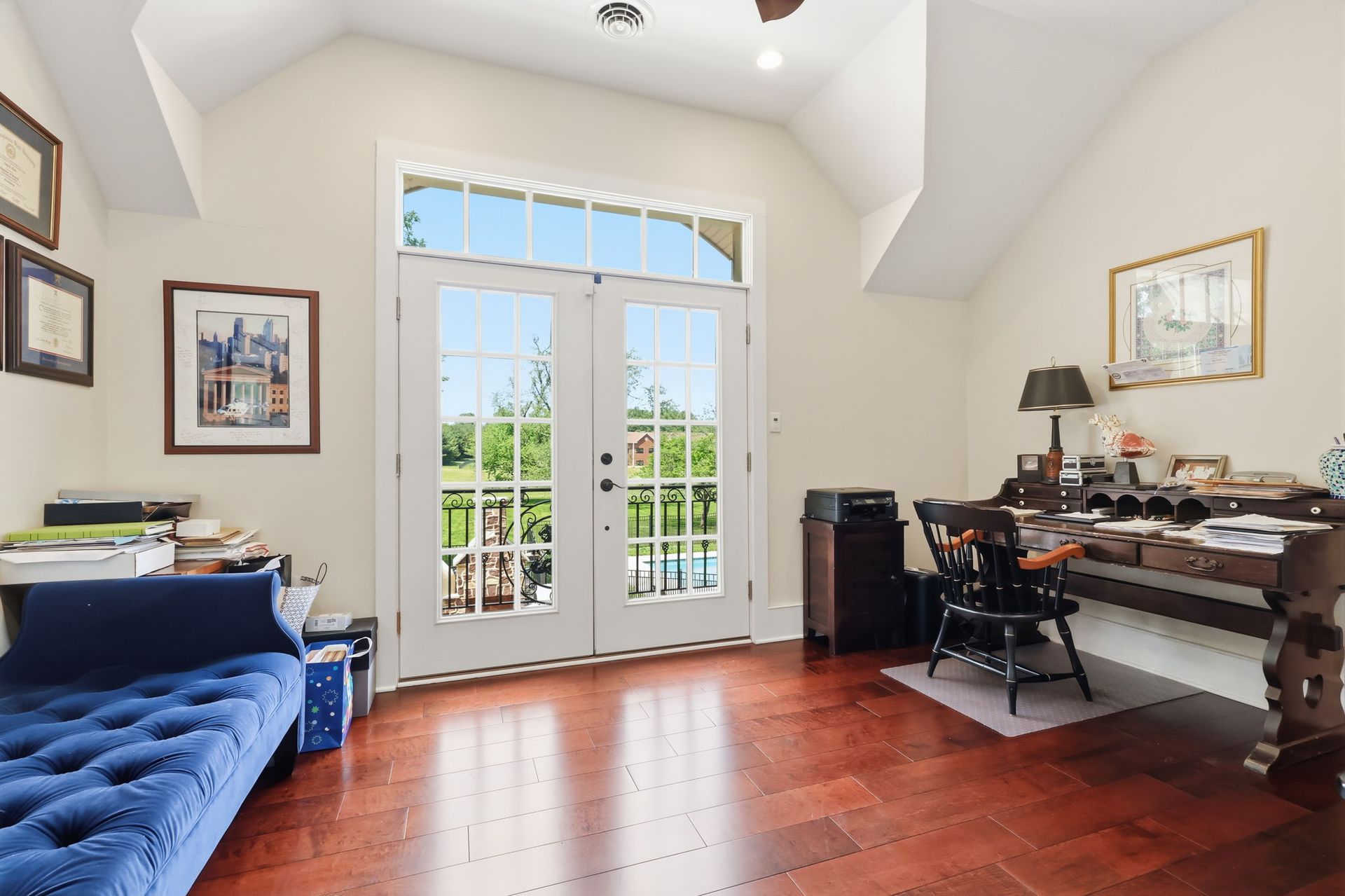 Home office with blue sofa, wood desk, and French doors opening to a bright patio