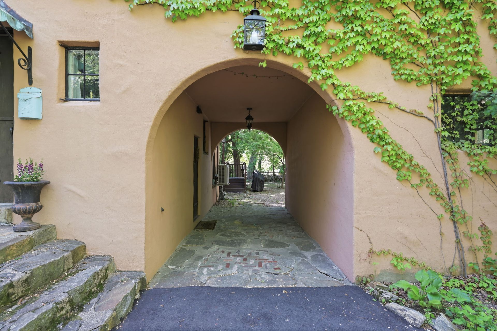 Arched stone passageway in a beige building, lined with ivy and leading to a courtyard beyond.