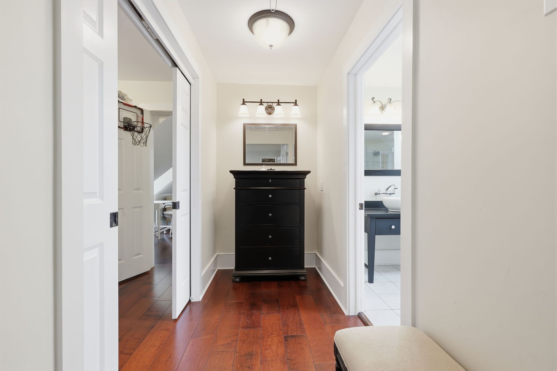 Narrow hallway with hardwood floors, a black dresser, and open doorways to a bathroom and kitchen