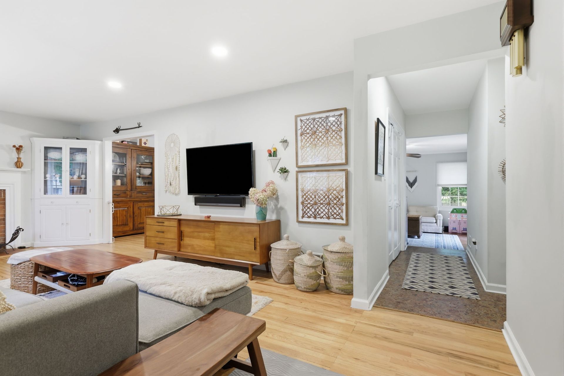 Bright living room with TV, wooden console, beige sofa, framed art, and hallway to a kitchen.