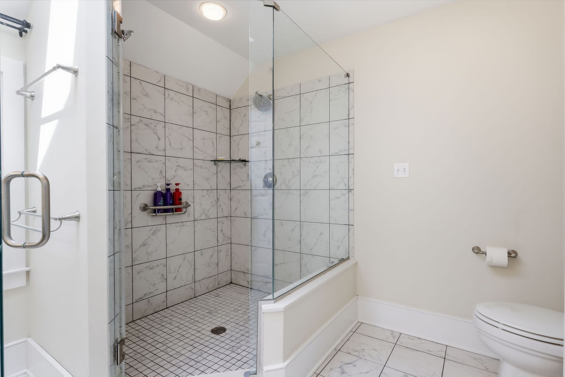 Bright modern bathroom with glass shower, white tile, and toilet