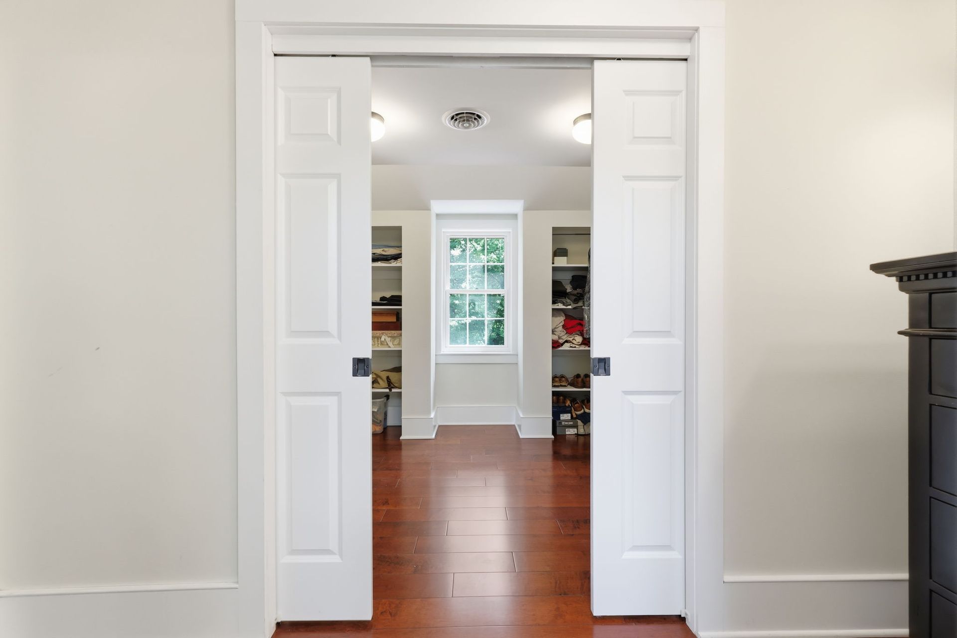 Open double doors framing a bright room with hardwood floors and a window at the far end.
