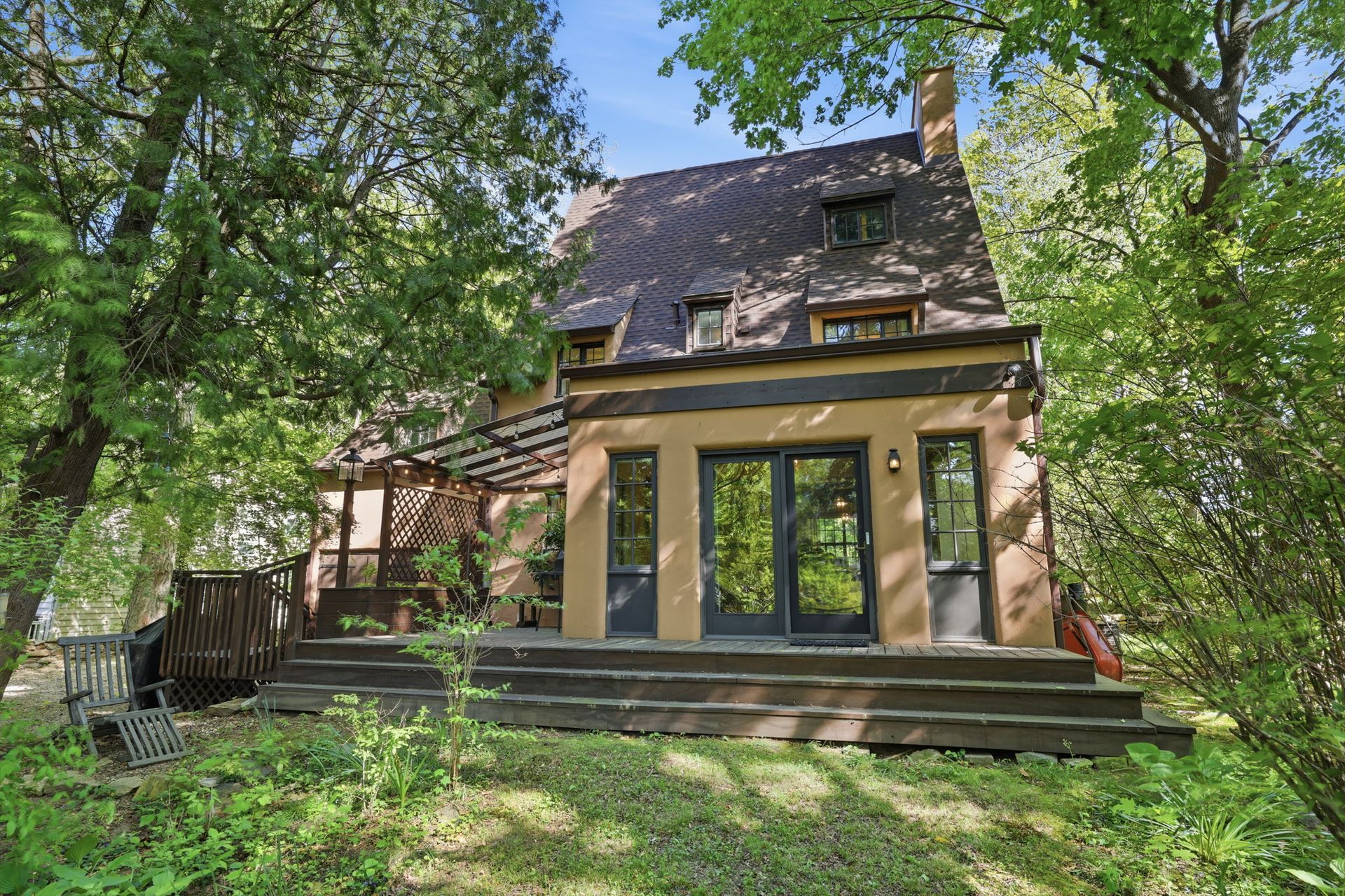 Stone house with large glass doors and a shaded front porch surrounded by trees and greenery