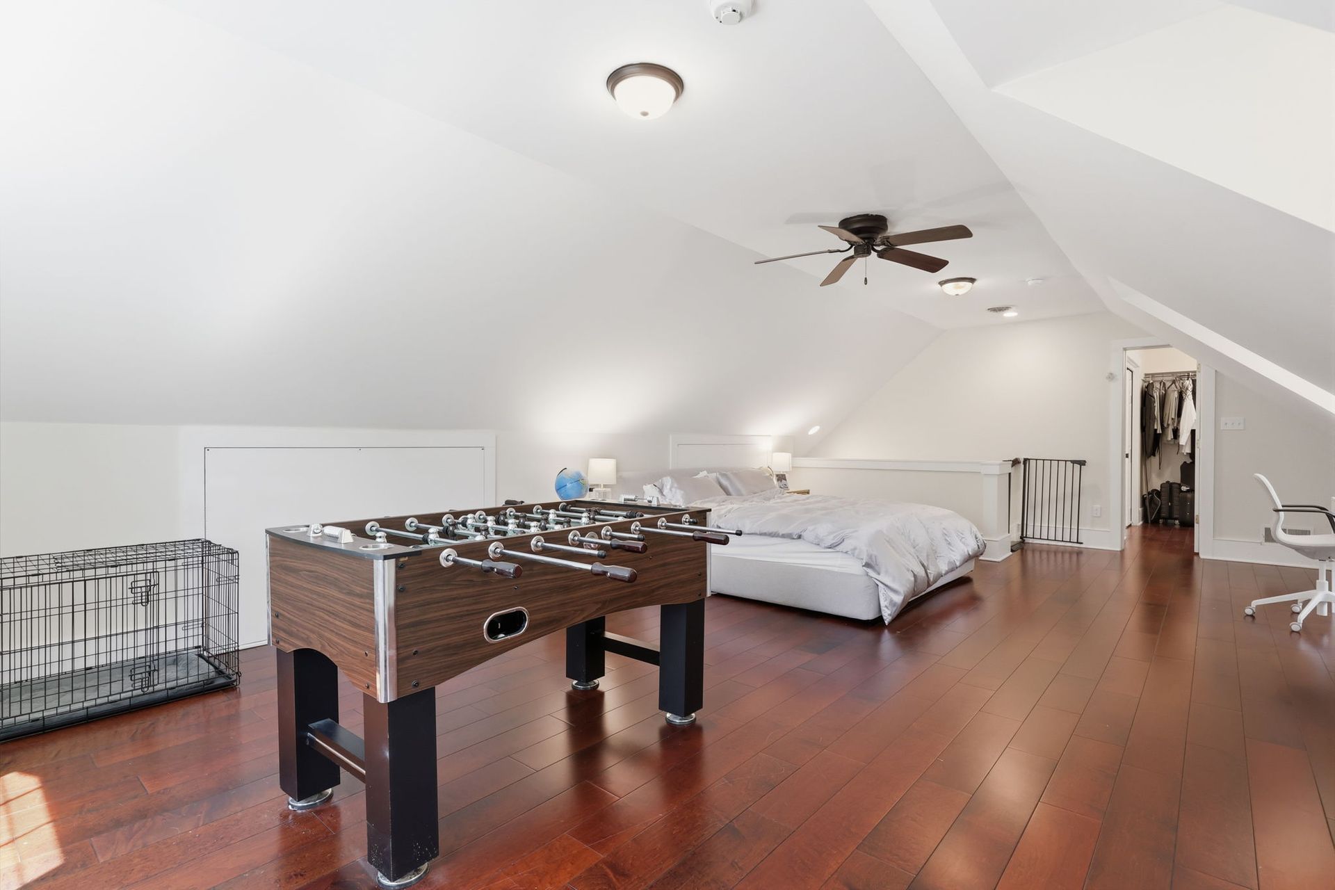 Spacious attic bedroom with wood floors, a bed, foosball table, and ceiling fan