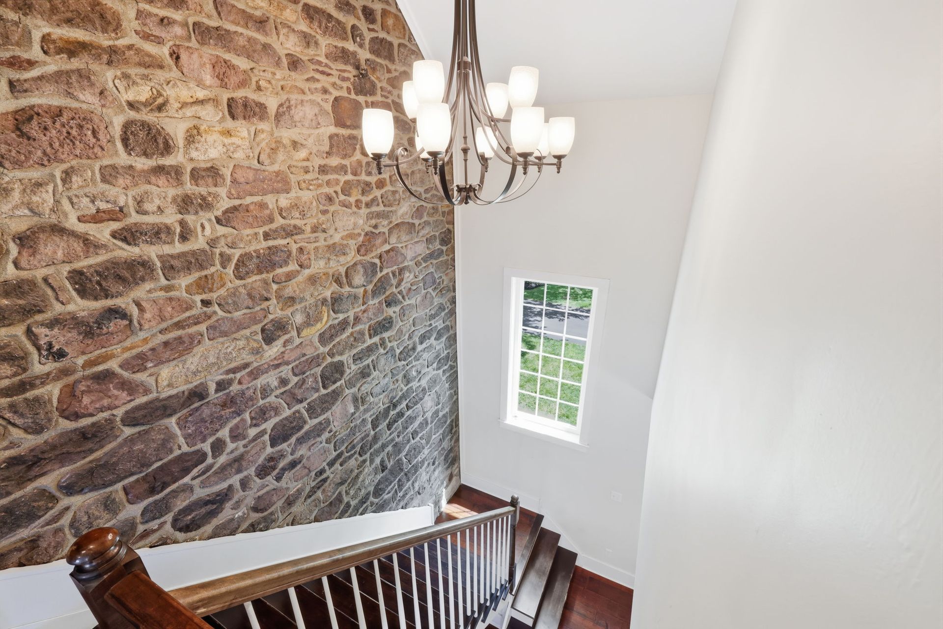 Stairwell with stone wall, white walls, chandelier, and a window.