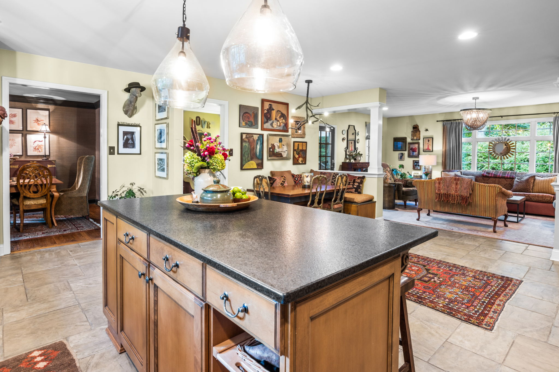 Kitchen with island, light fixtures, and doorways leading to dining and living areas, decorated with art.