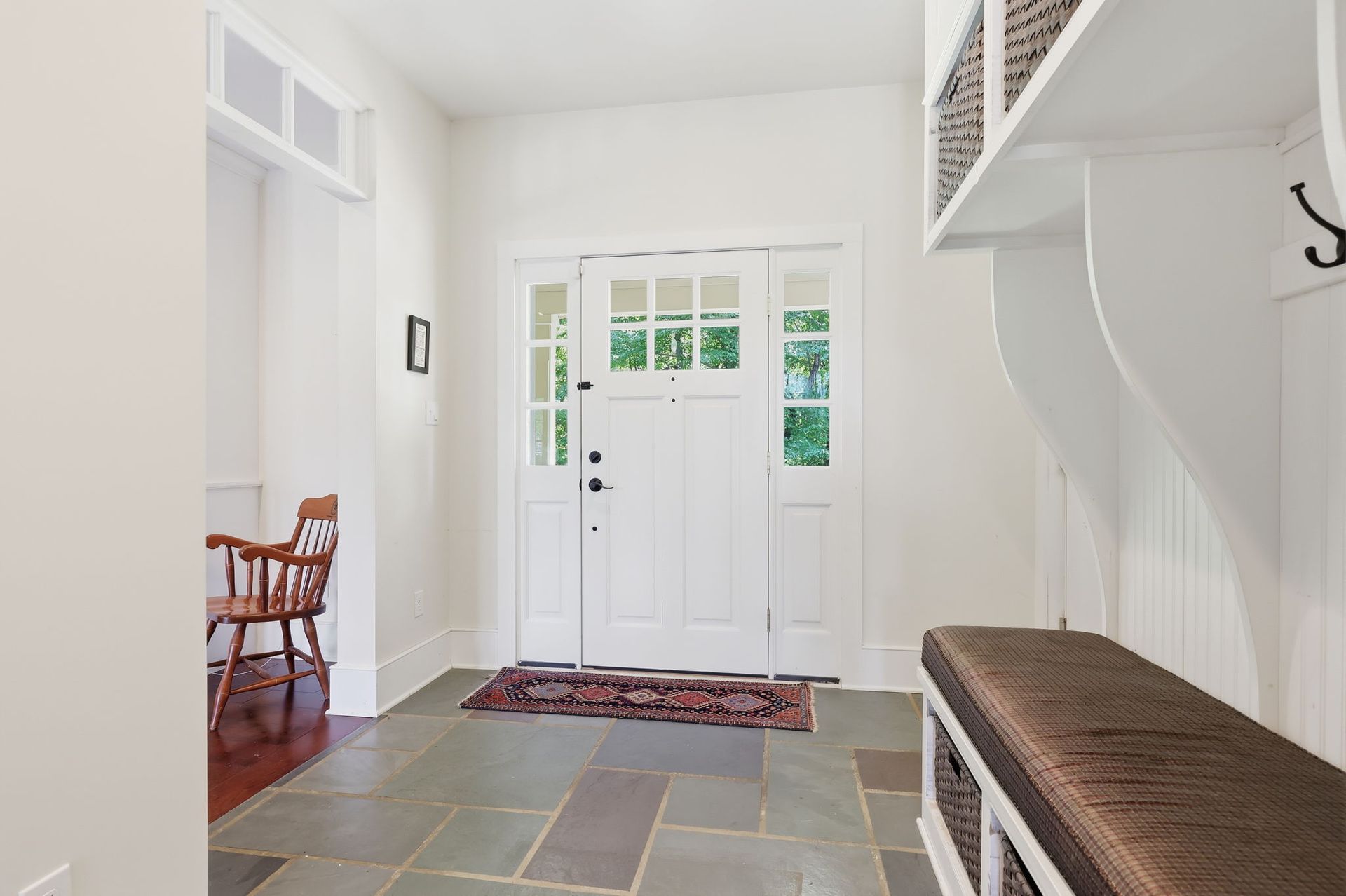 Front entryway with white door, slate tile floor, bench, and small wooden chairs.
