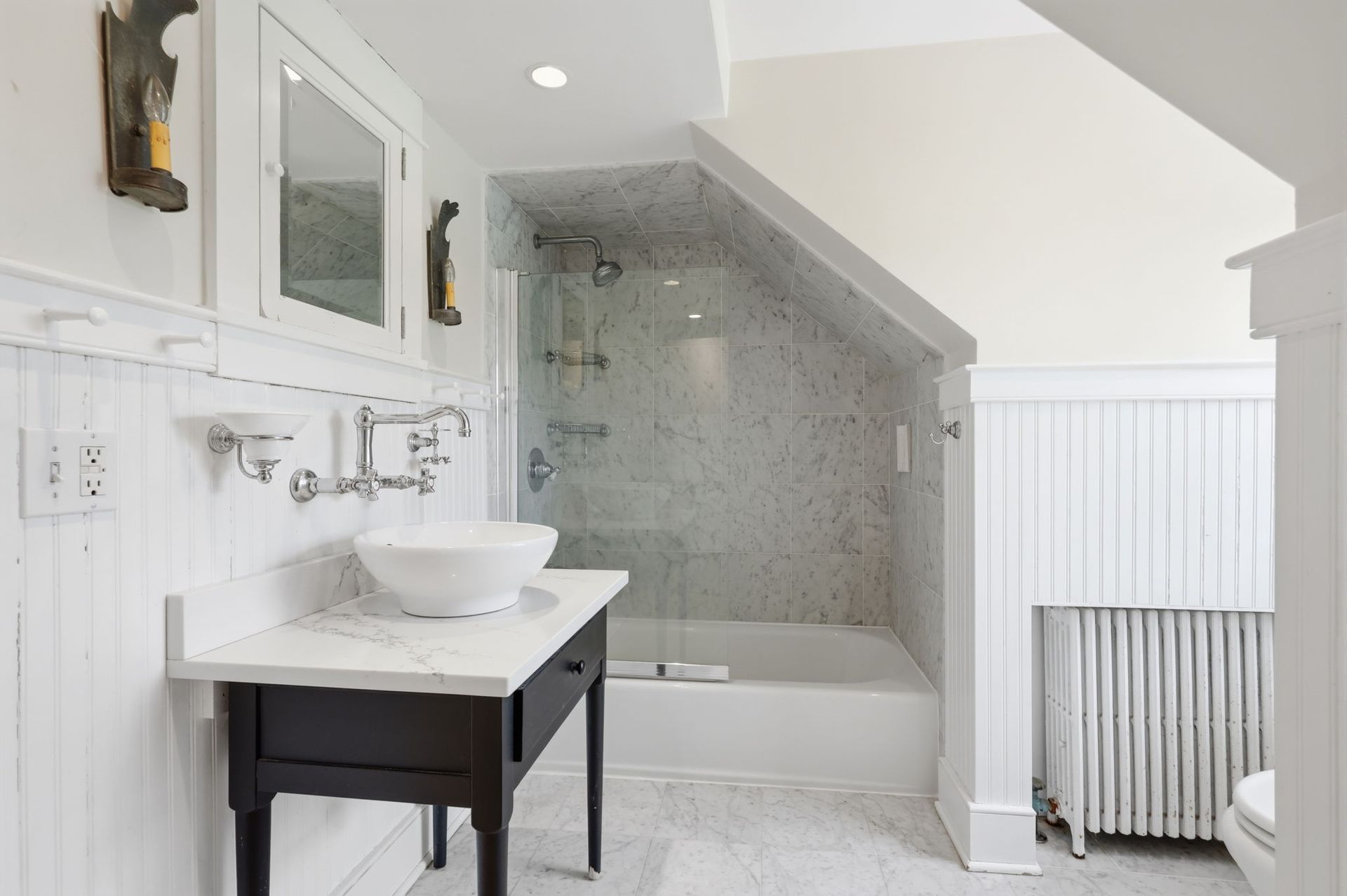 Bright bathroom with white vanity, black sink cabinet, and a tiled walk-in shower under a sloped ceiling