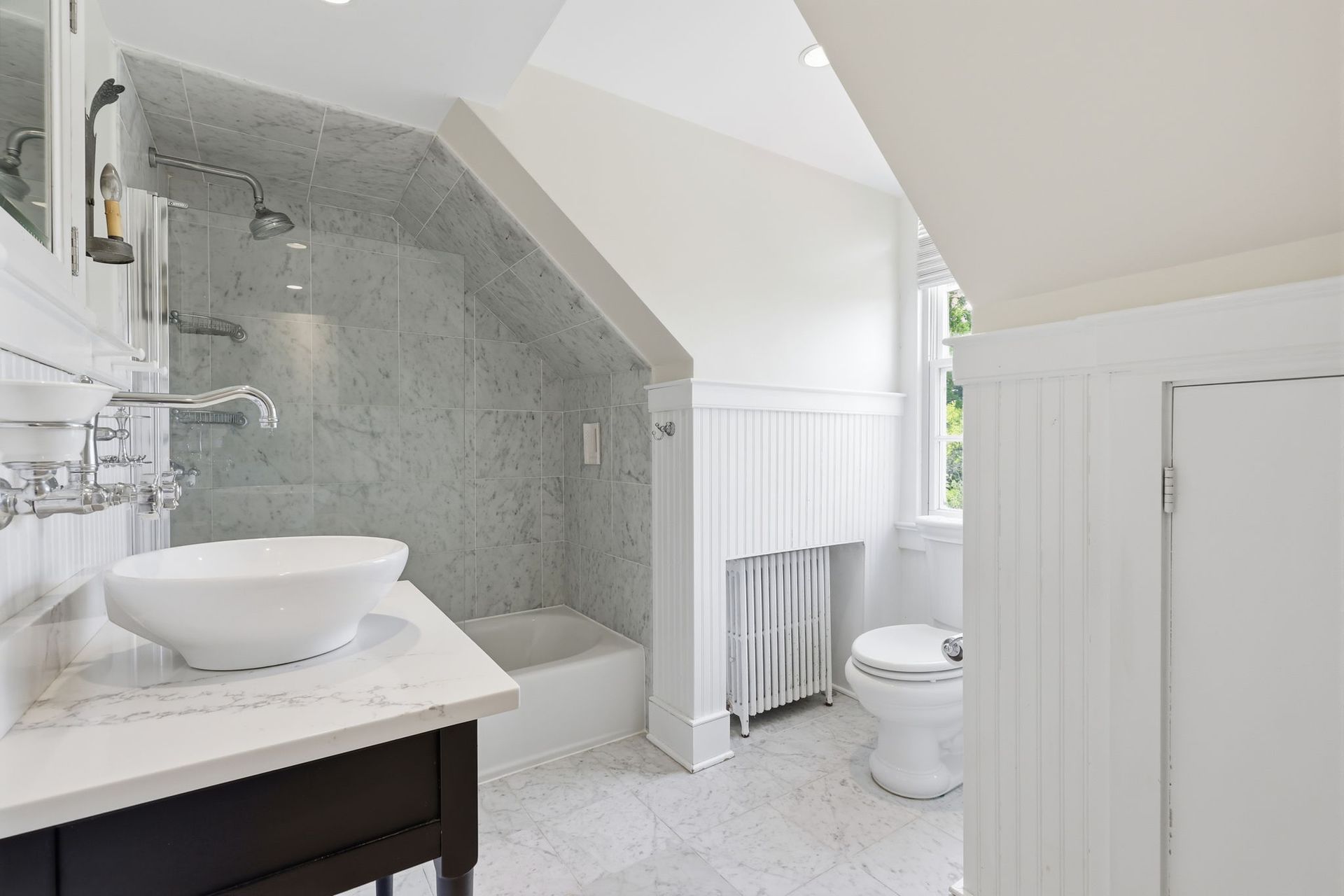 Bright white bathroom with tiled shower, pedestal sink, and toilet under sloped ceiling.