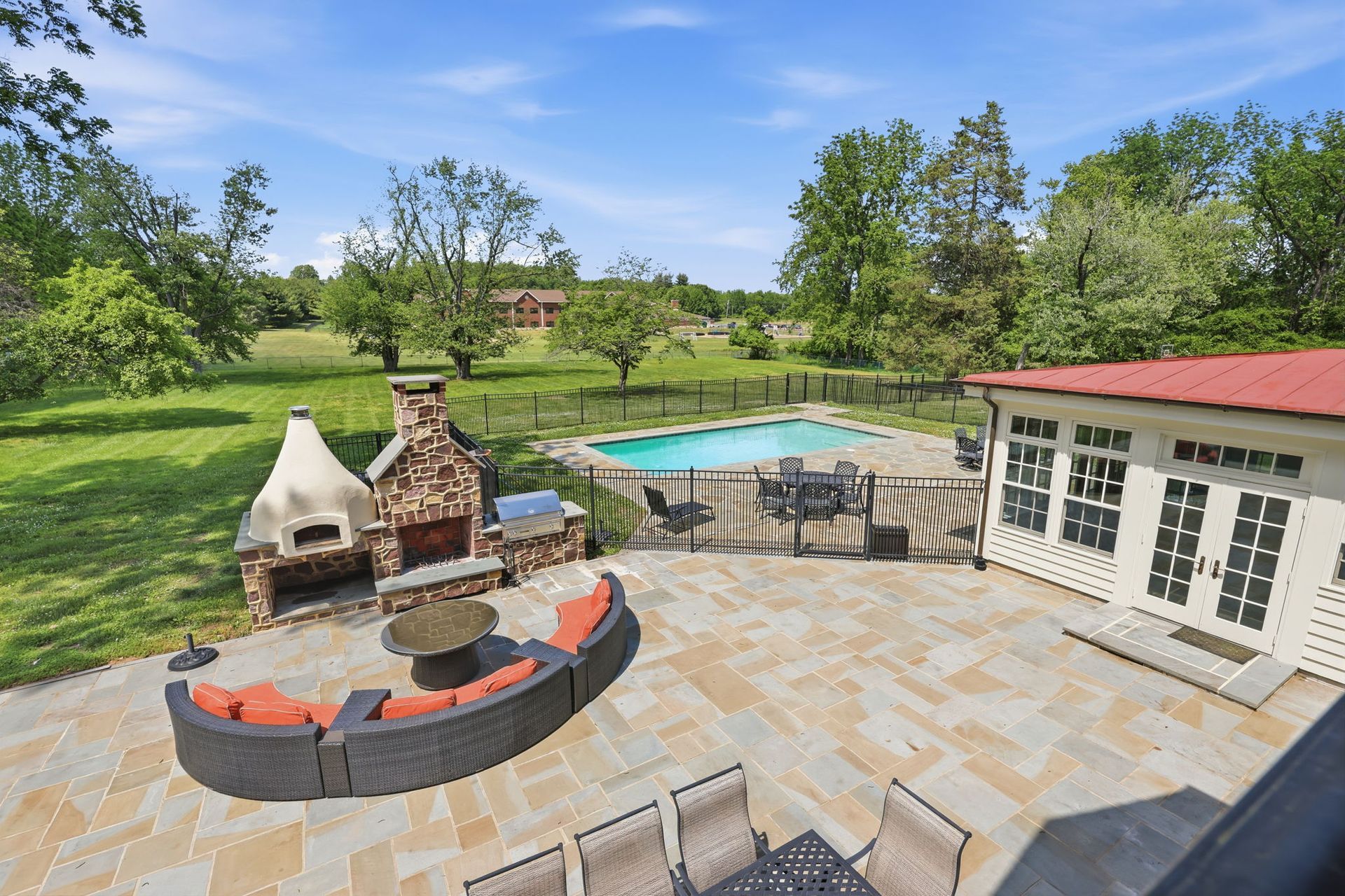 Patio with fire pit, grill, and pool overlooking a green garden and trees