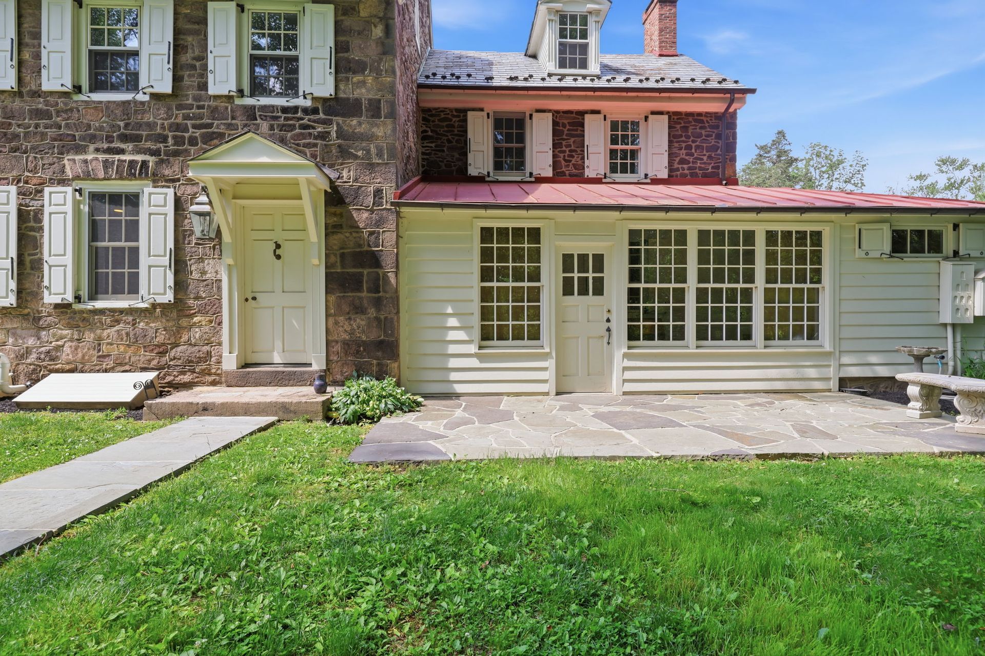 Front view of a brick and cream house with white shutters, a green lawn, and a small covered porch.