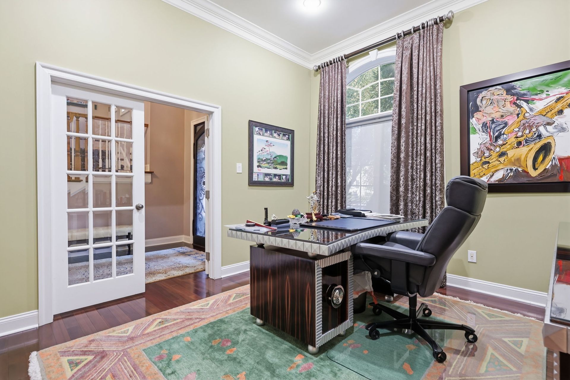 Home office with desk, black chair, patterned rug, and French doors to a bathroom.
