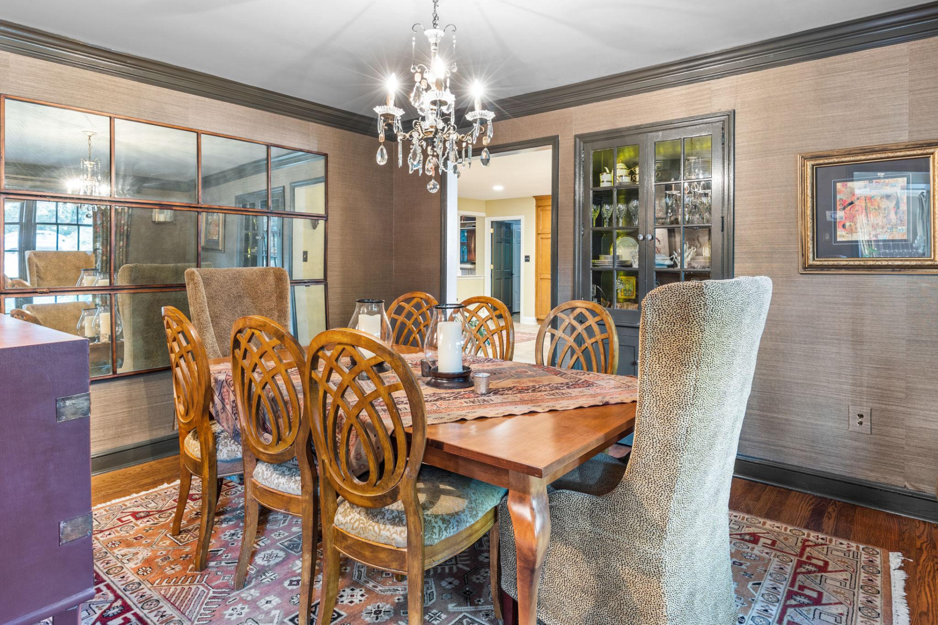 Formal dining room with wood table, patterned chairs, ornate chandelier, and large mirror.