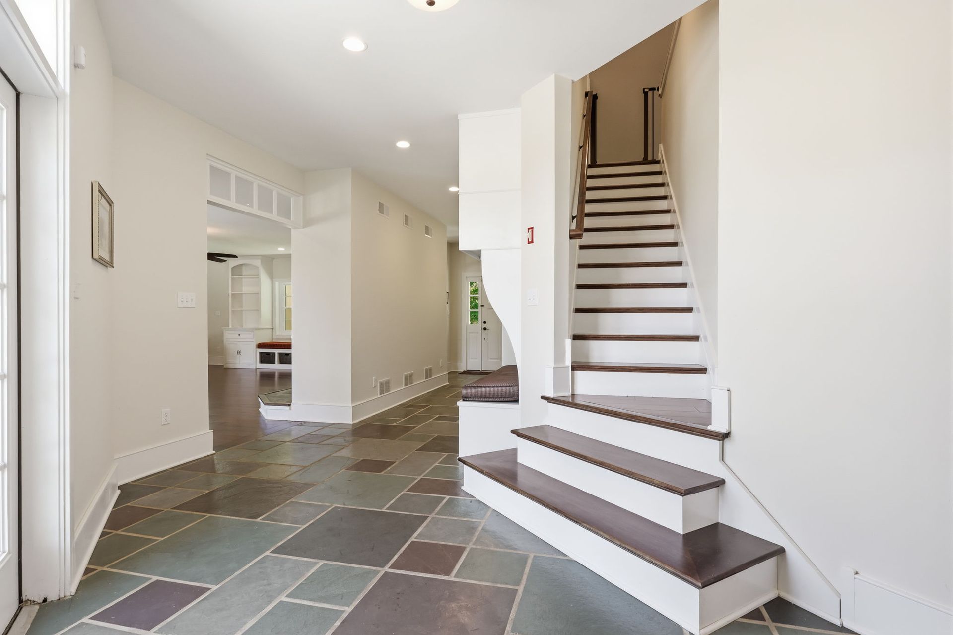 Bright entry hall with slate tile floor and white staircase leading upstairs