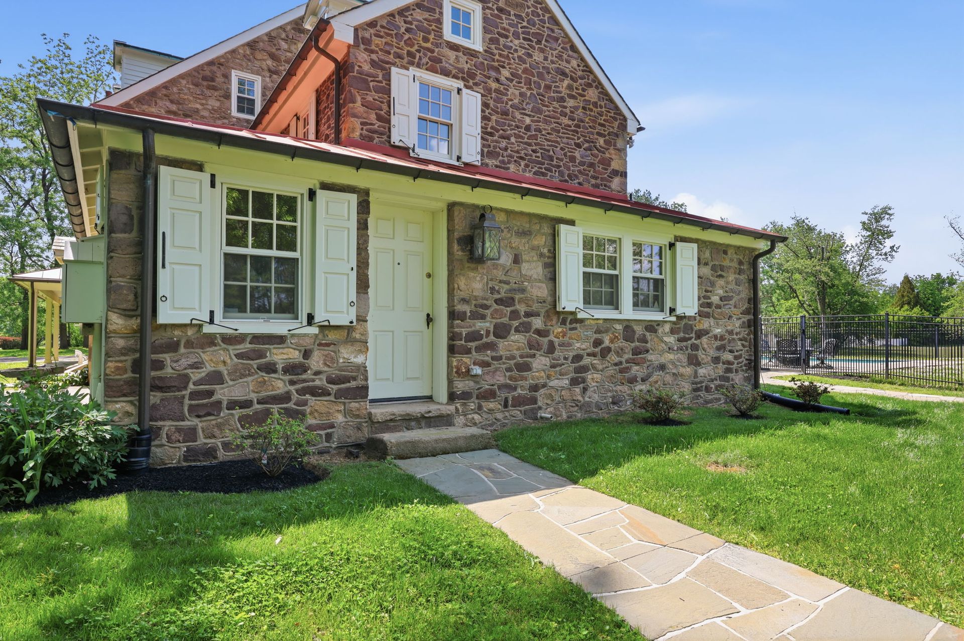 Stone house with white shutters, front door, and a stone walkway across a green lawn