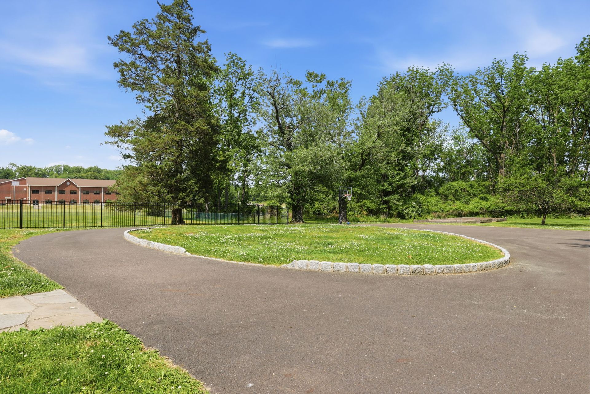 Curving paved path around a grassy island with trees under a bright blue sky