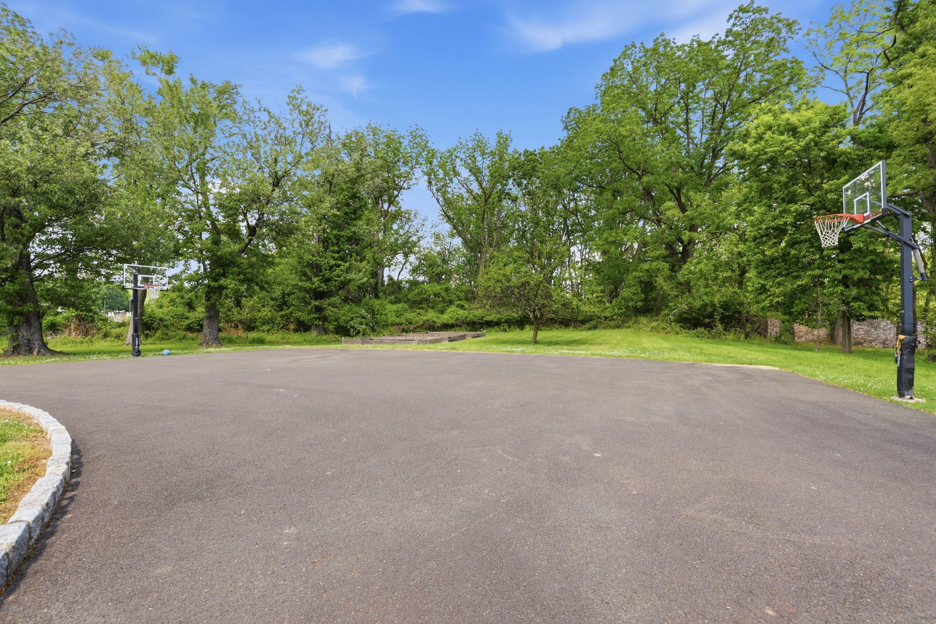 Empty outdoor basketball court surrounded by trees under a clear blue sky
