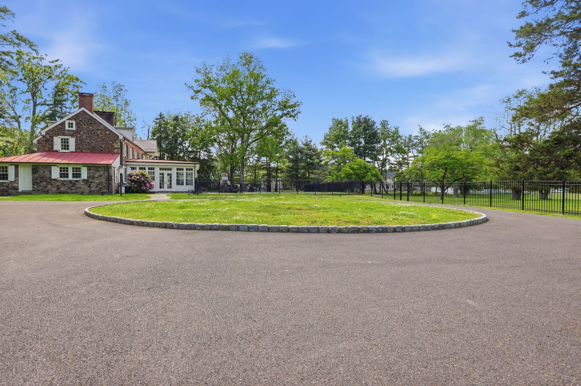 Country house with a gravel driveway, circular flower bed, and green trees under a blue sky