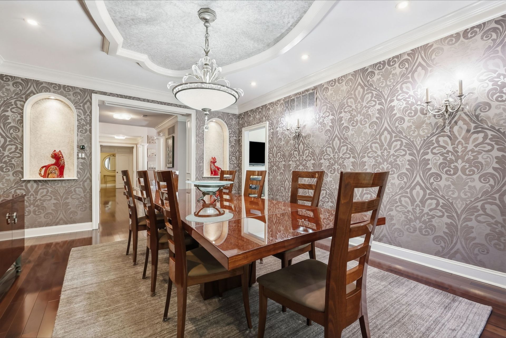Elegant dining room with glass table, wooden chairs, chandelier, and patterned wallpaper