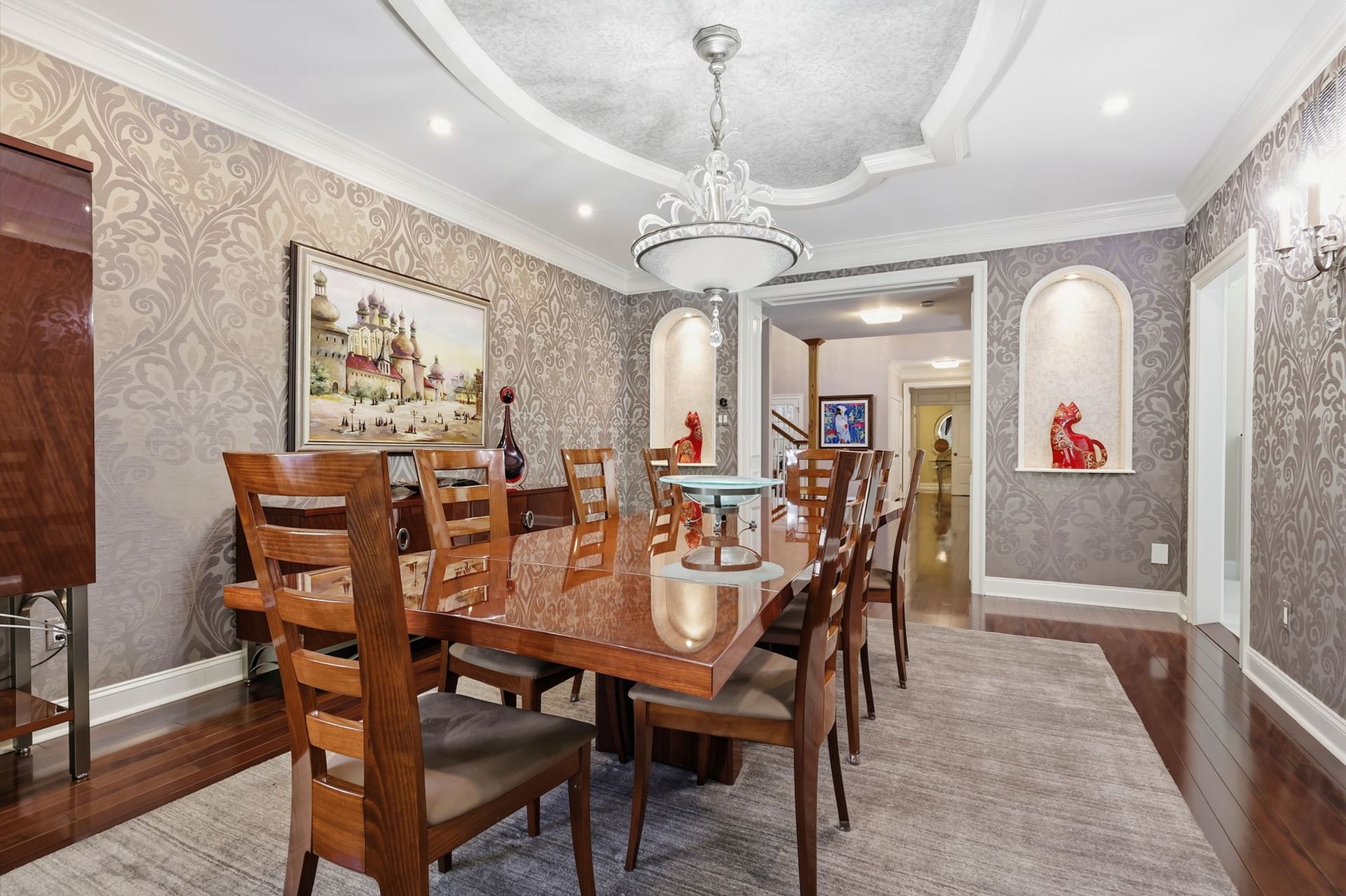 Elegant dining room with wooden table, chairs, chandelier, and arched wall niches.