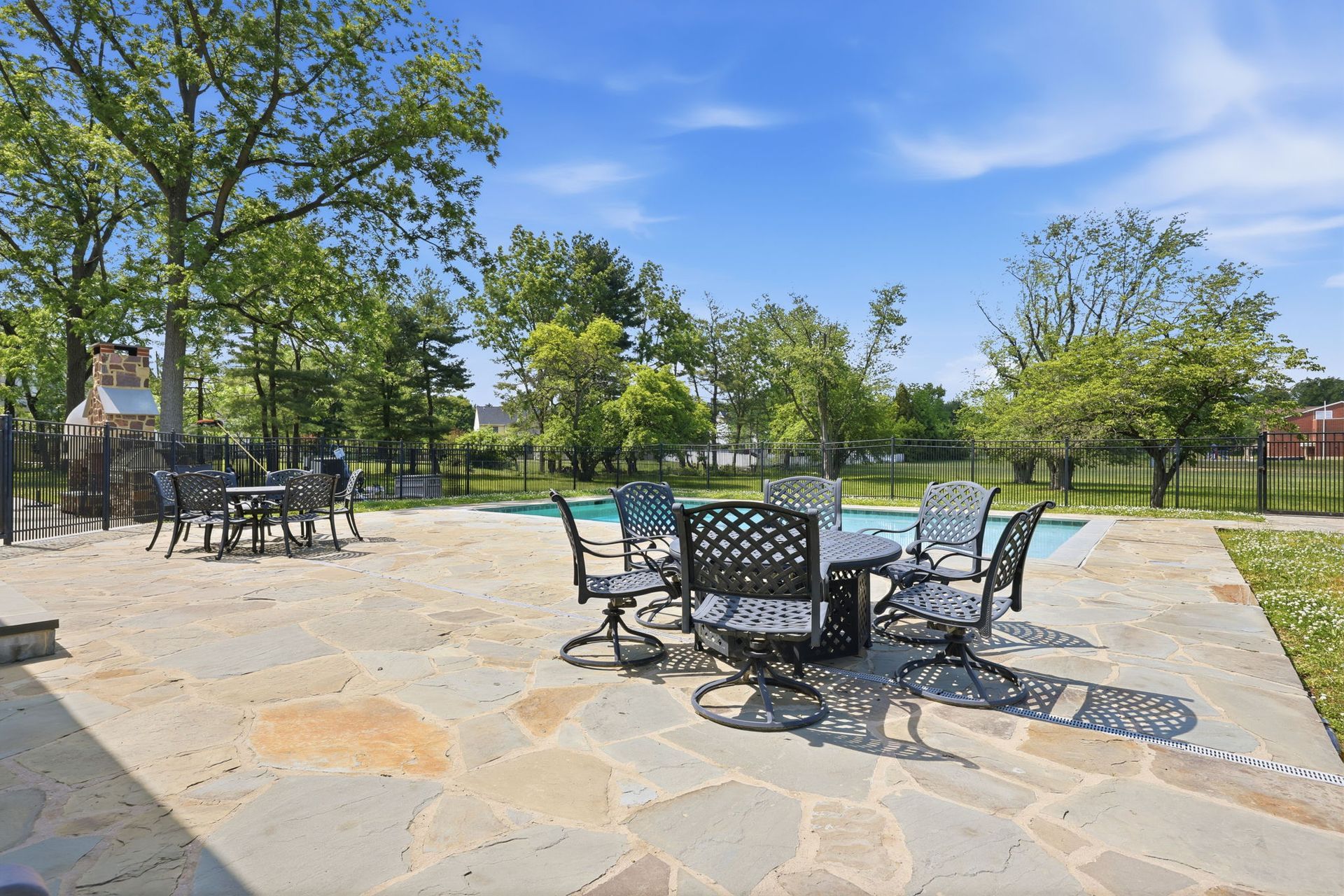Sunny park patio with black metal tables and chairs on a stone terrace, trees and a playground in the background