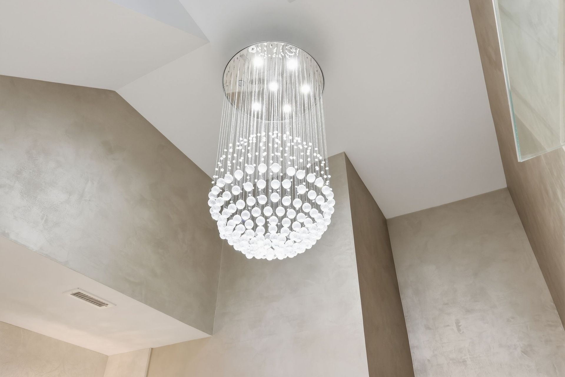 Crystal chandelier hanging from a high beige ceiling in a modern interior room