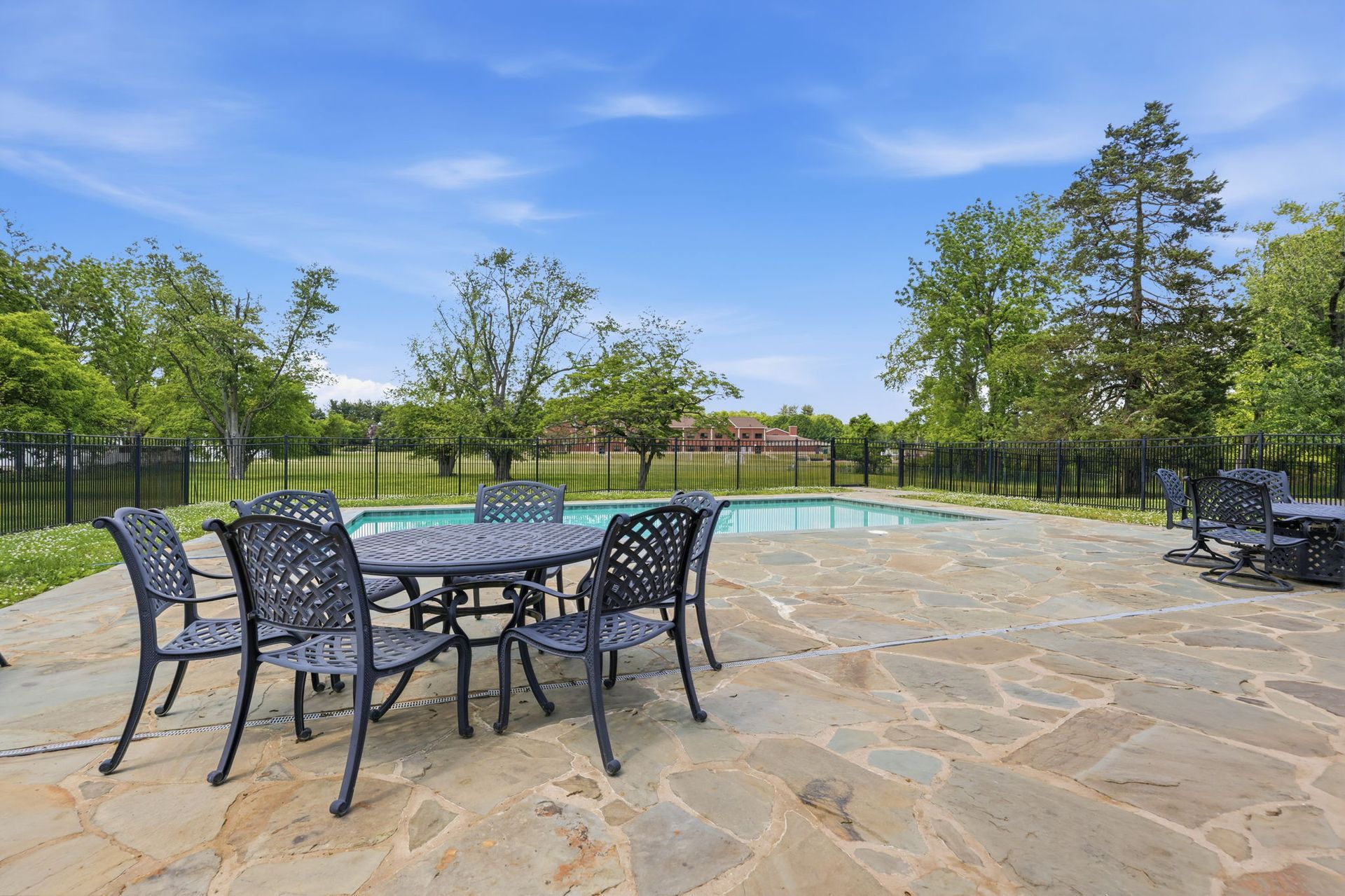 Patio with black metal table and chairs on a stone terrace overlooking a green landscape under a blue sky
