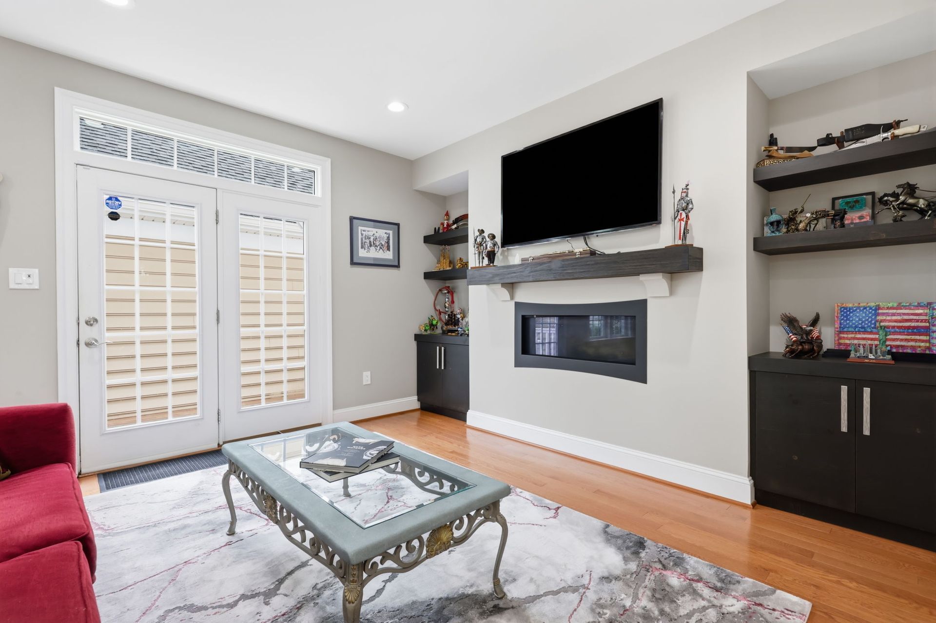 Bright living room with a fireplace, wall-mounted TV, glass coffee table, and French doors to a patio.