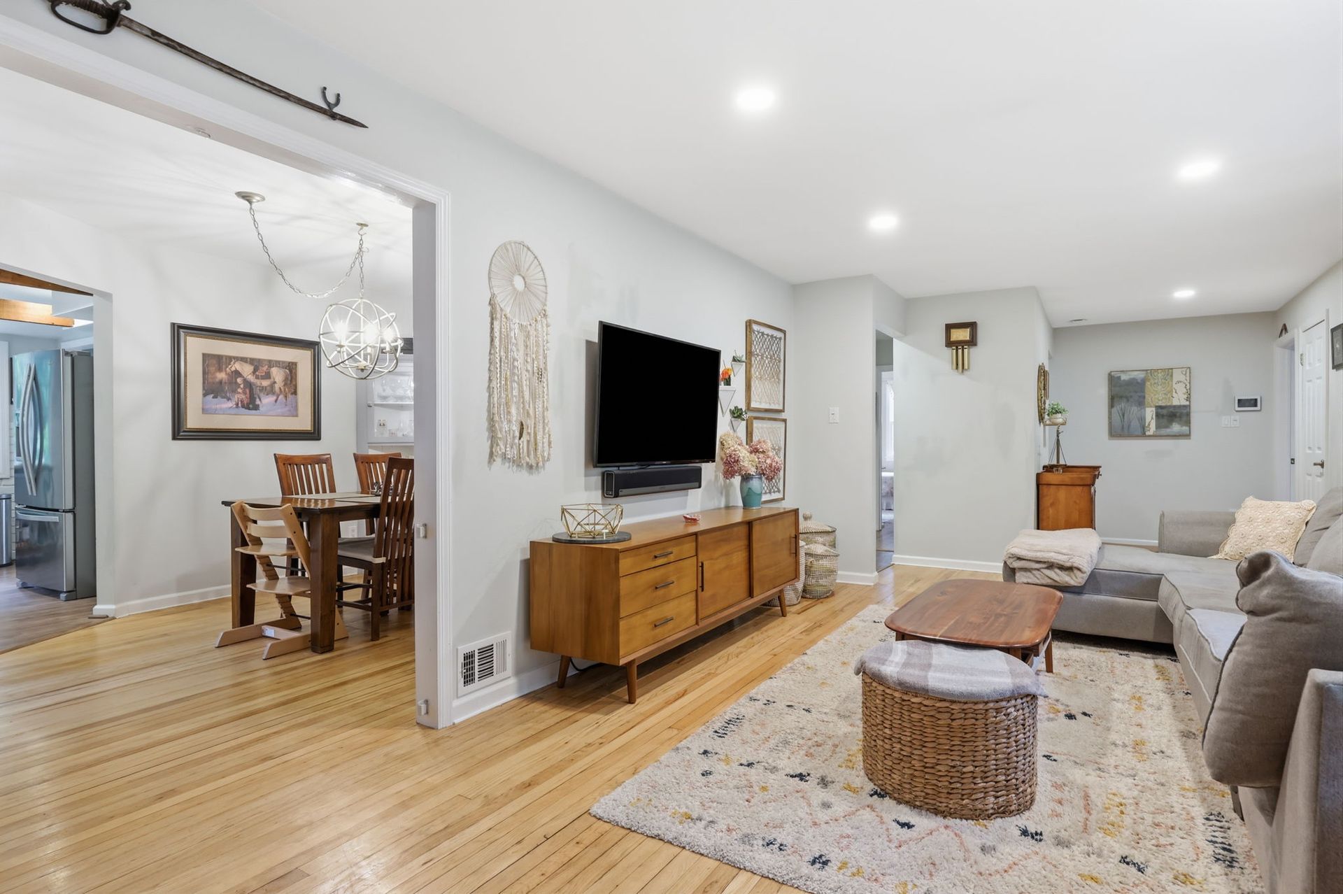 Bright living room with gray sofa, TV on wooden console, patterned rug, and adjoining dining area